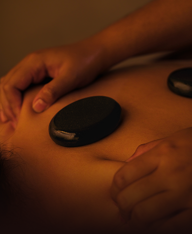 Close-up of a person receiving a hot stone massage, with smooth black stones placed on their back.