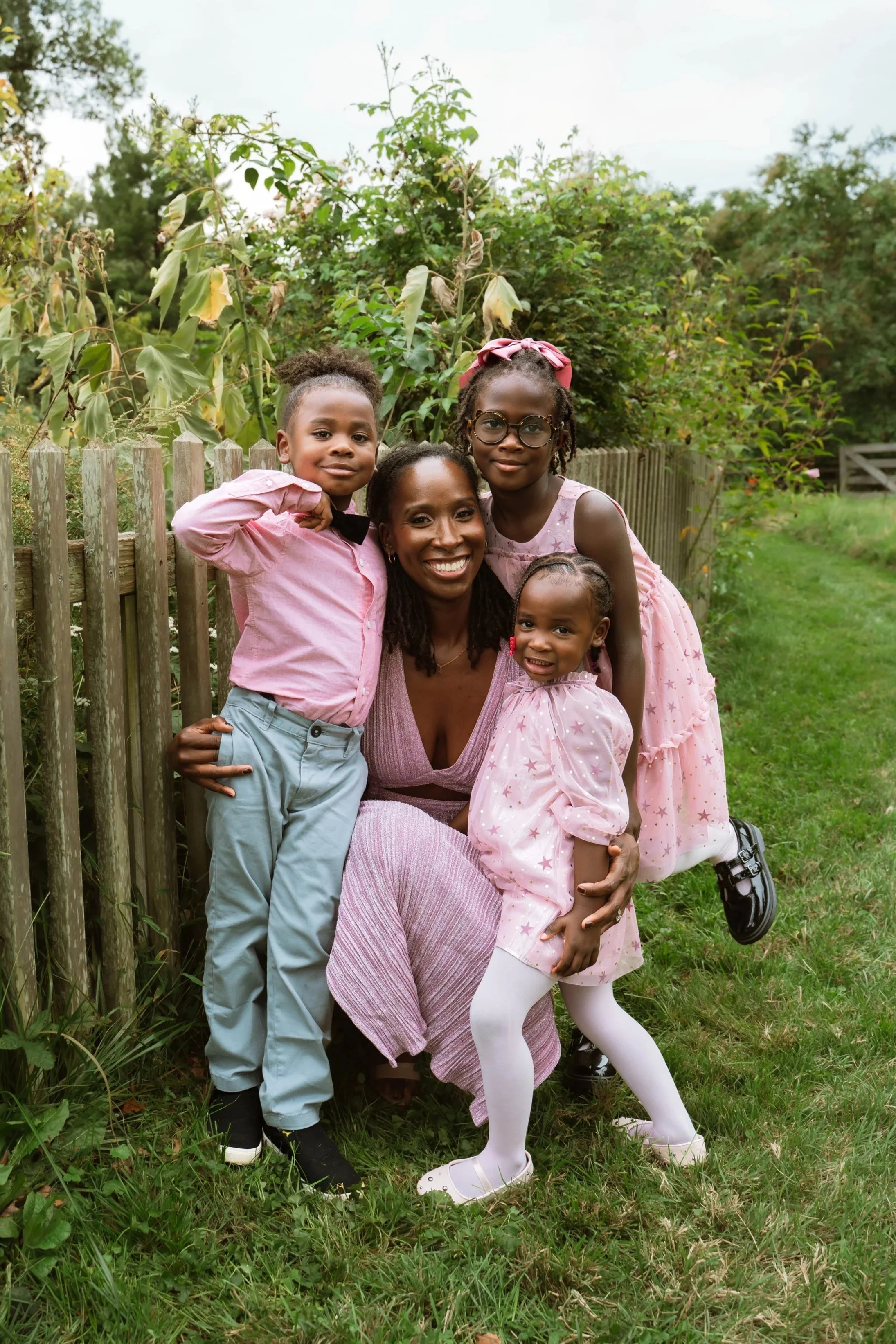 Black mother with three children wearing pink talking about life and lactation. Family is smiling with green forest background.
