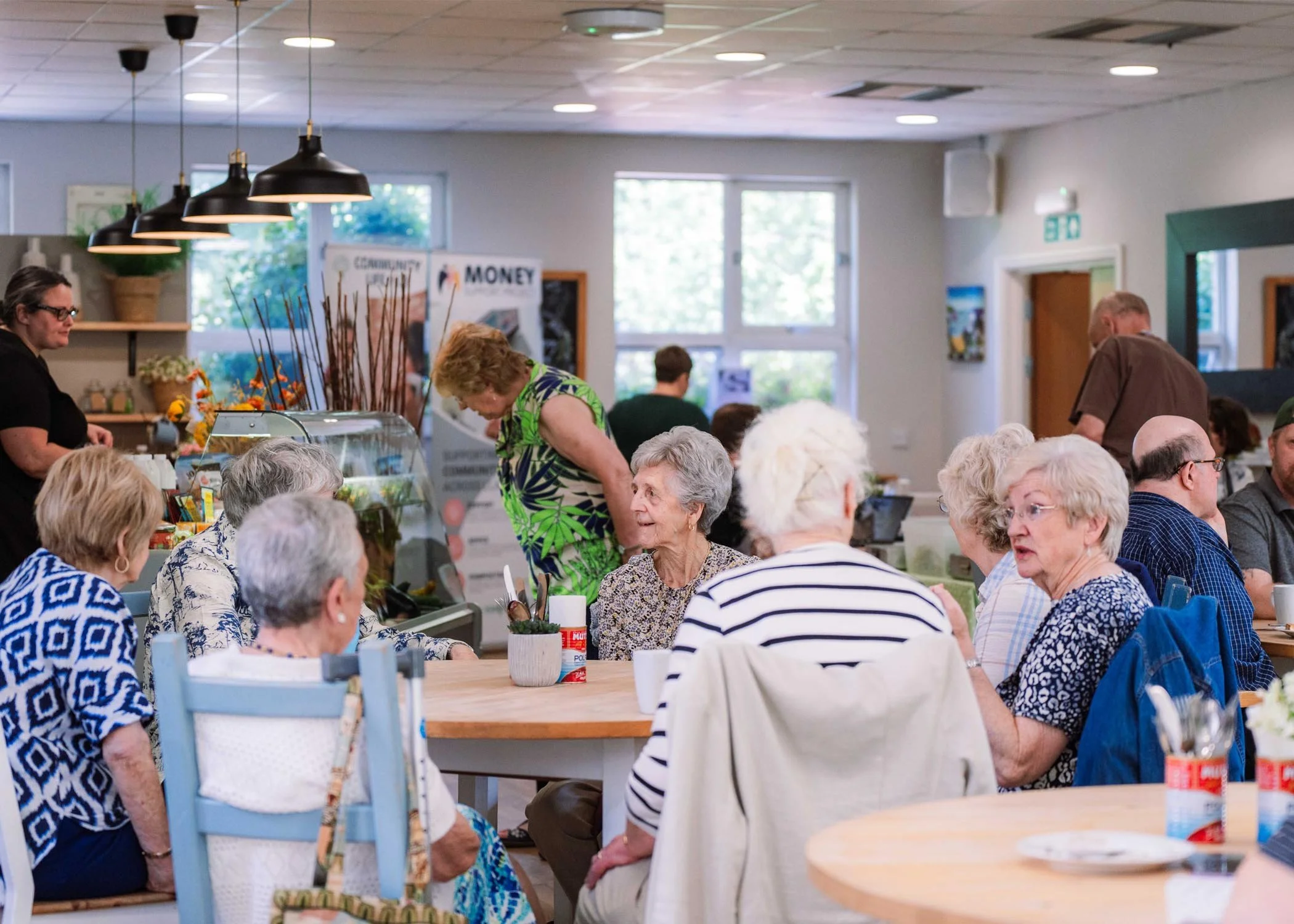 Elderly people sitting at tables in a bright cafe or community center.