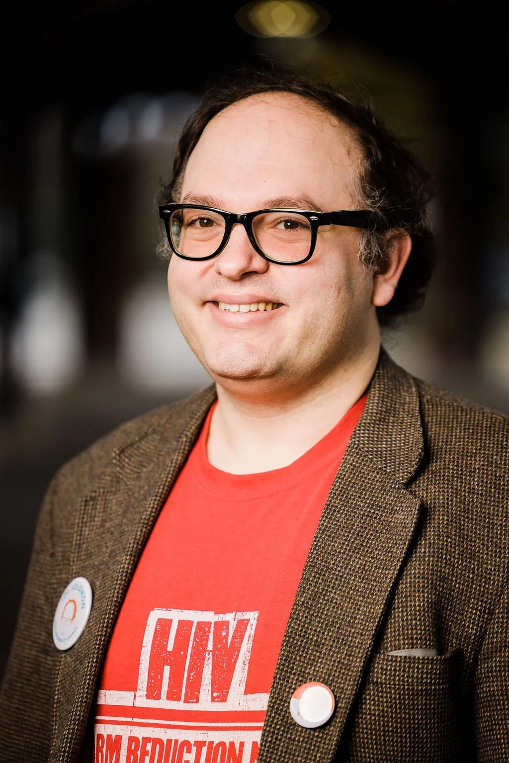 Man wearing red shirt, brown blazer, and black rimmed glasses