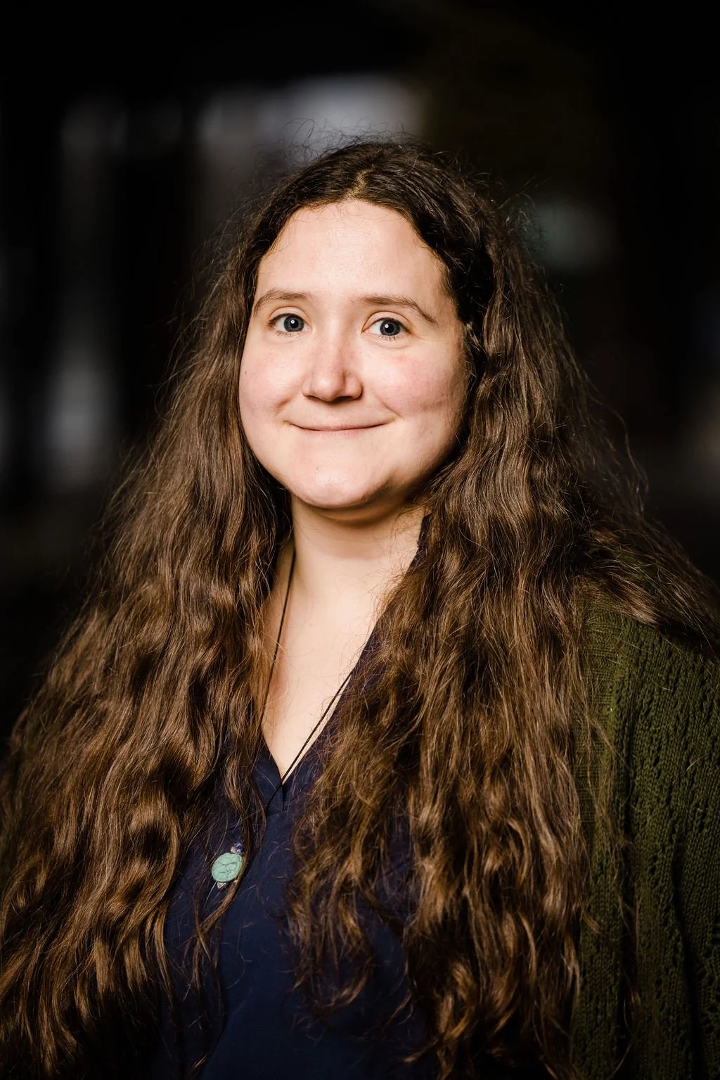 Woman with long brown hair wearing blue shirt, turquoise necklace and green cardigan