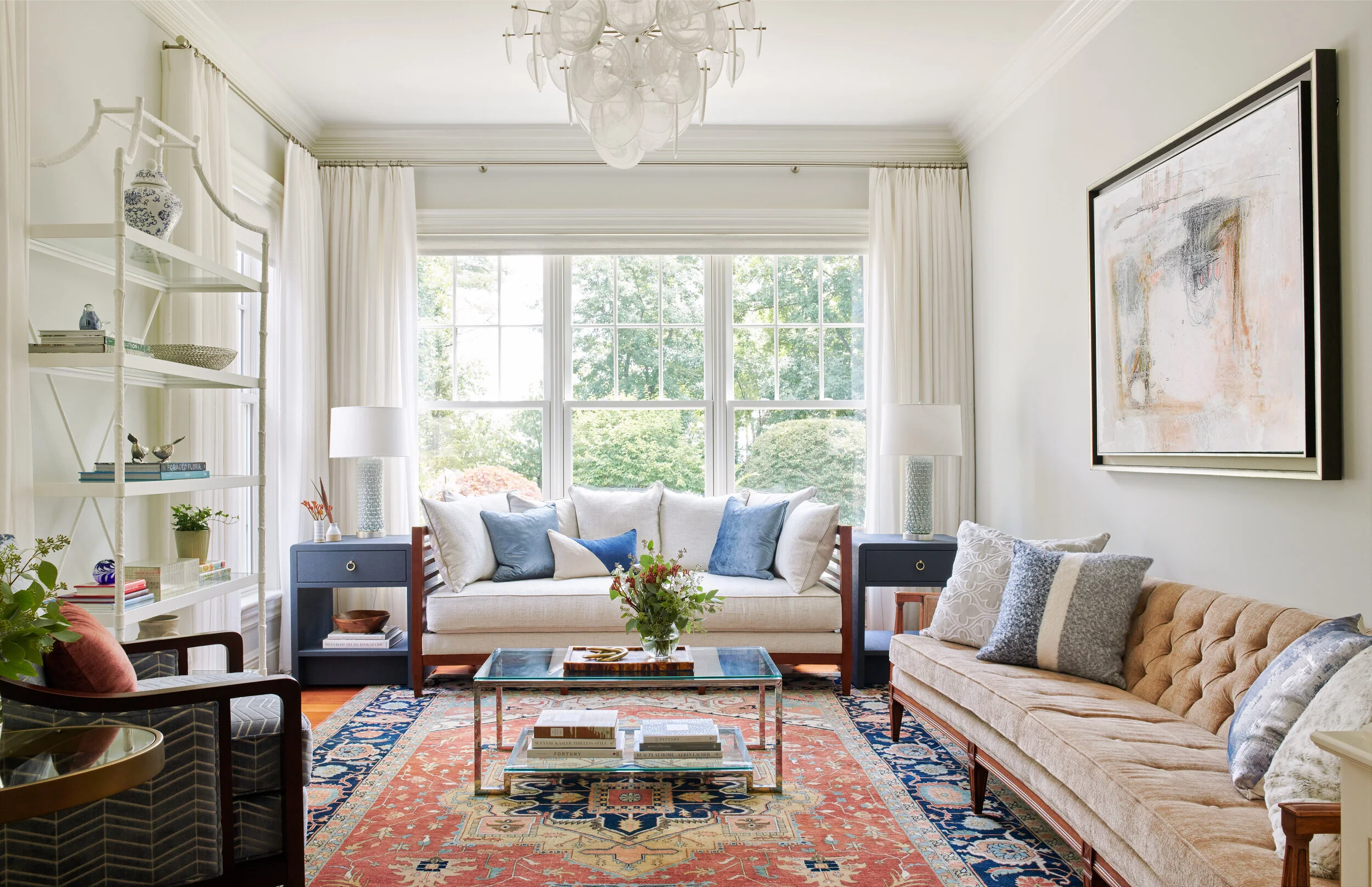 Bright living room featuring layered vintage and modern furnishings, patterned rug, neutral sofas, and blue accents, designed by Georgia Zikas and featured in Mansion Global.