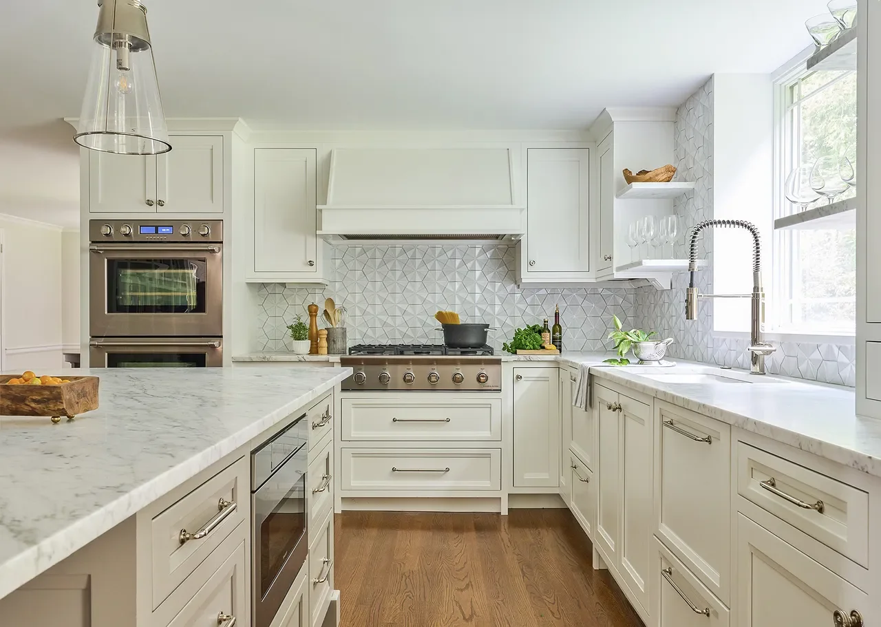 Traditional white kitchen with shaker cabinets, marble countertops, geometric tile backsplash, and warm wood flooring creating a timeless and inviting design.
