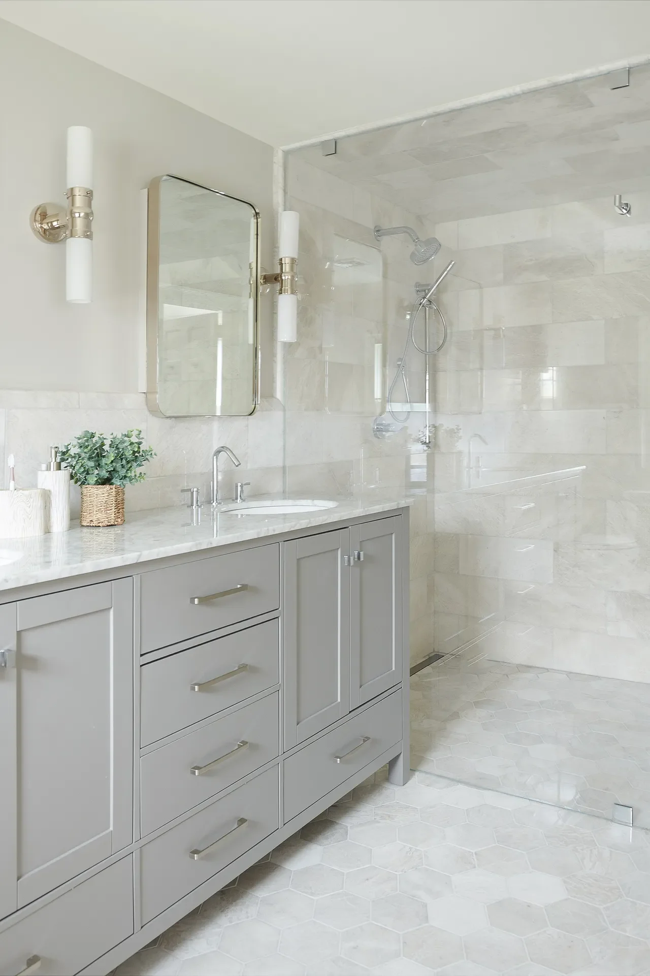 Grey and white bathroom with a shaker-style vanity, marble countertop, hex tile flooring, and glass-enclosed shower with light stone tile for a clean, layered look.