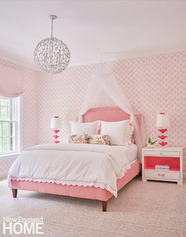Pink girls bedroom with patterned wallpaper, canopy bed, matching lamps, and layered white bedding designed by Georgia Zikas.