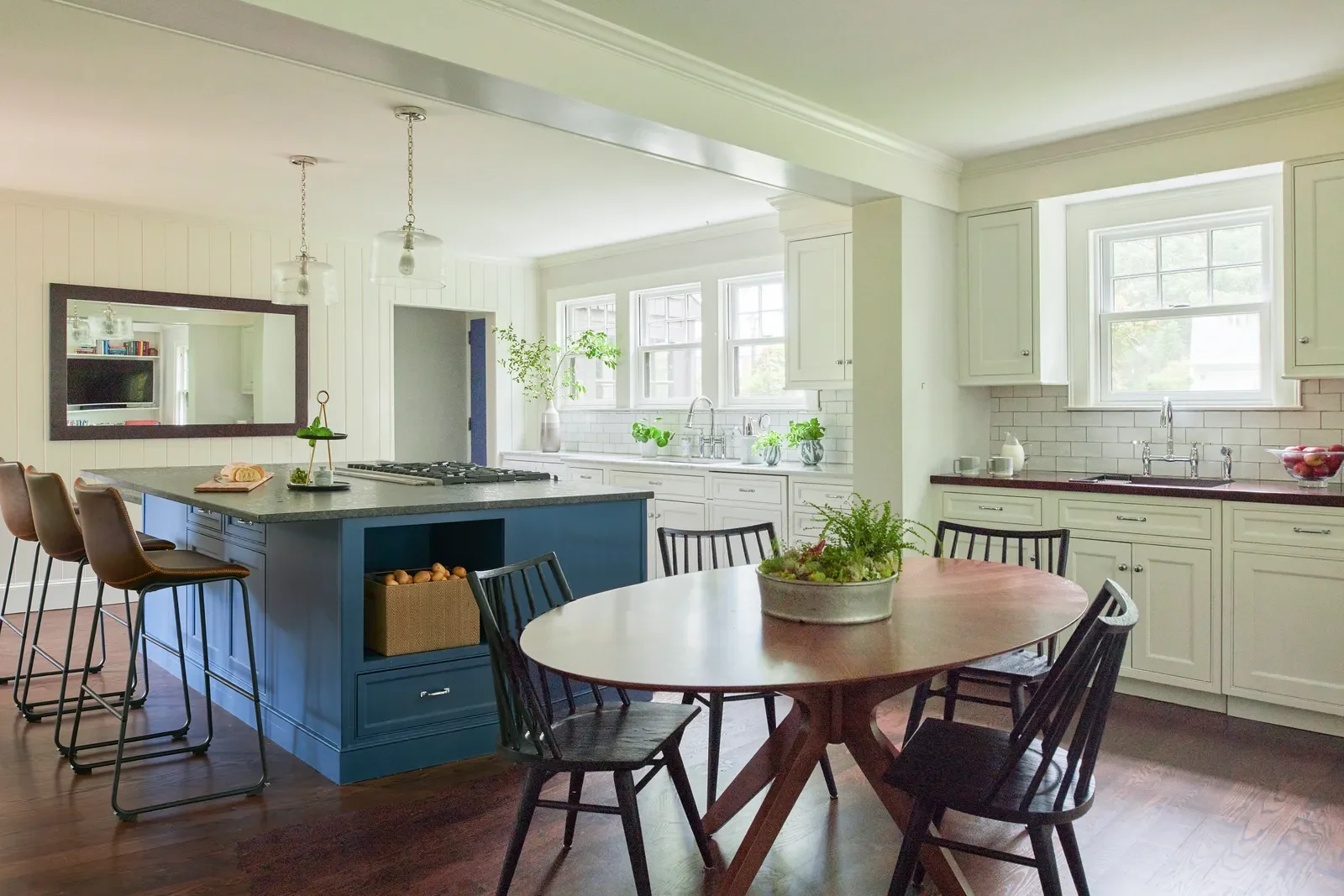 Bright kitchen designed by Georgia Zikas with a navy blue island, white shaker cabinets, marble countertops, and wood accents, featured in Architectural Digest’s kitchen cabinet paint trends article.