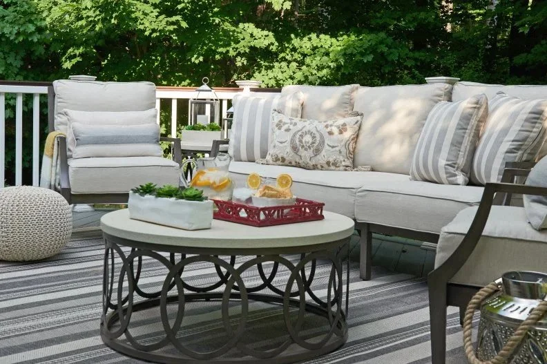 Cozy outdoor patio seating area with cushioned chairs, striped pillows, a round metal coffee table, and refreshments displayed on a red tray, designed by Georgia Zikas Design.