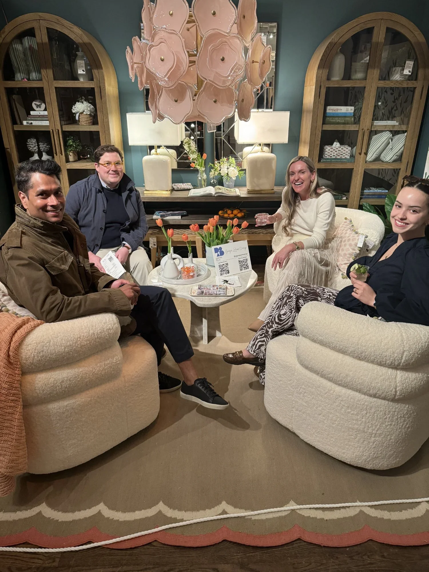 Georgia Zikas and three guests sit in a cozy vignette at Design on a Dime 2024, surrounded by boucle swivel chairs, tulip arrangements, layered decor, and a sculptural pink chandelier.