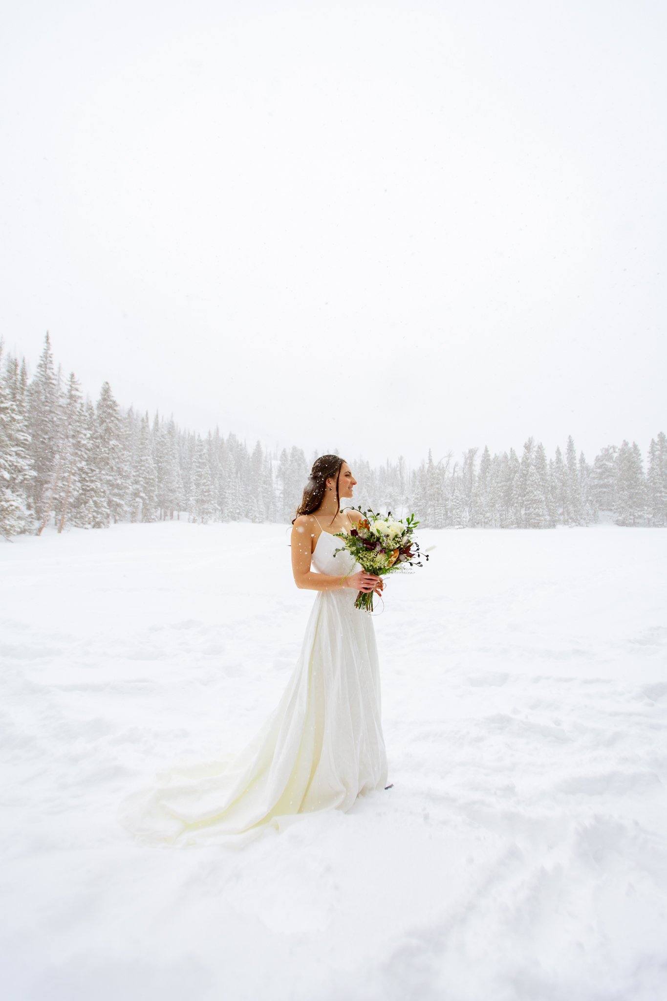  Bride stands with her bouquet in the middle of a frozen lake in her white dress for her elopement at Rocky Mountain National Park 