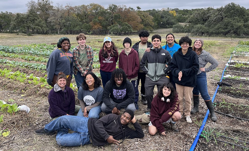 Group of young people in the fields, some standing and some sitting, smiling and posing for a photo.