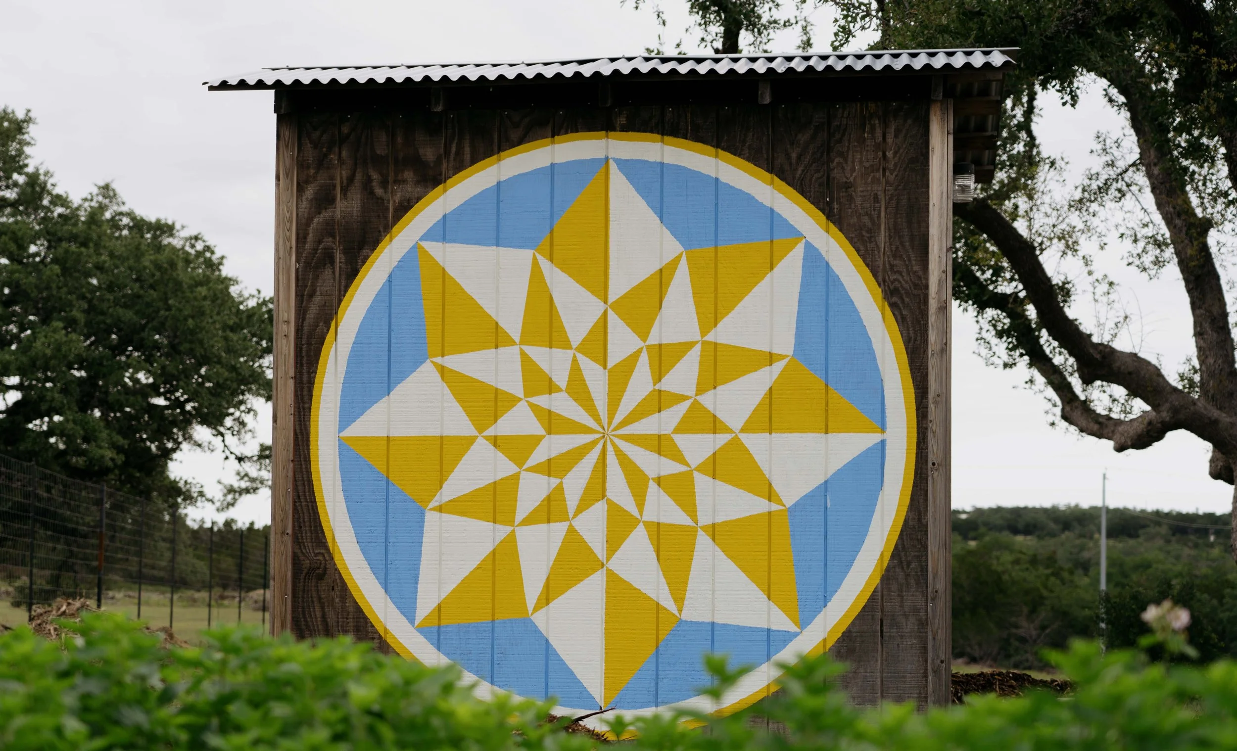 Large wooden structure with a circular geometric art design painted on it, featuring yellow, white, and light blue colors in a star pattern.