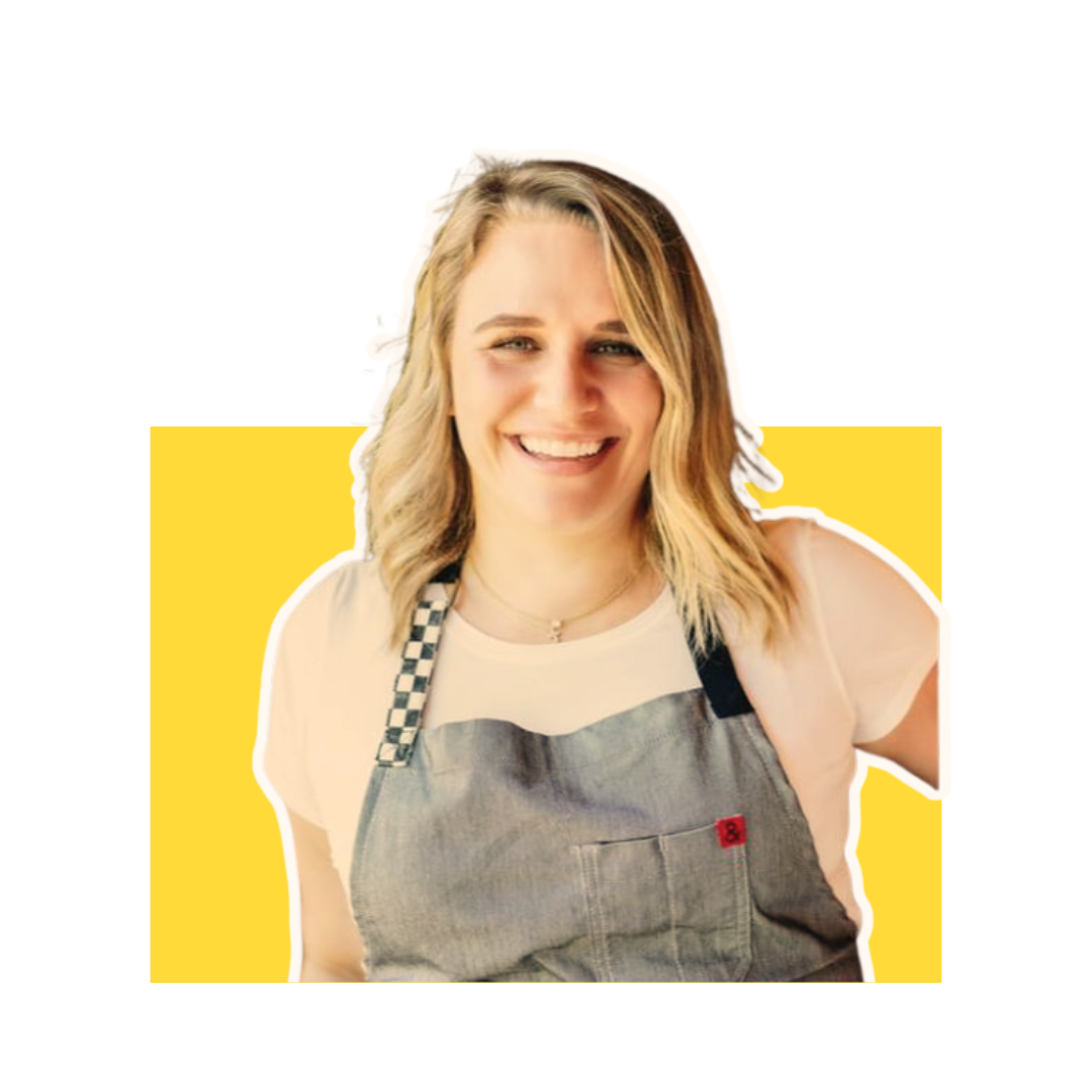 Smiling young woman with blonde hair wearing a checkered apron over a white t-shirt.
