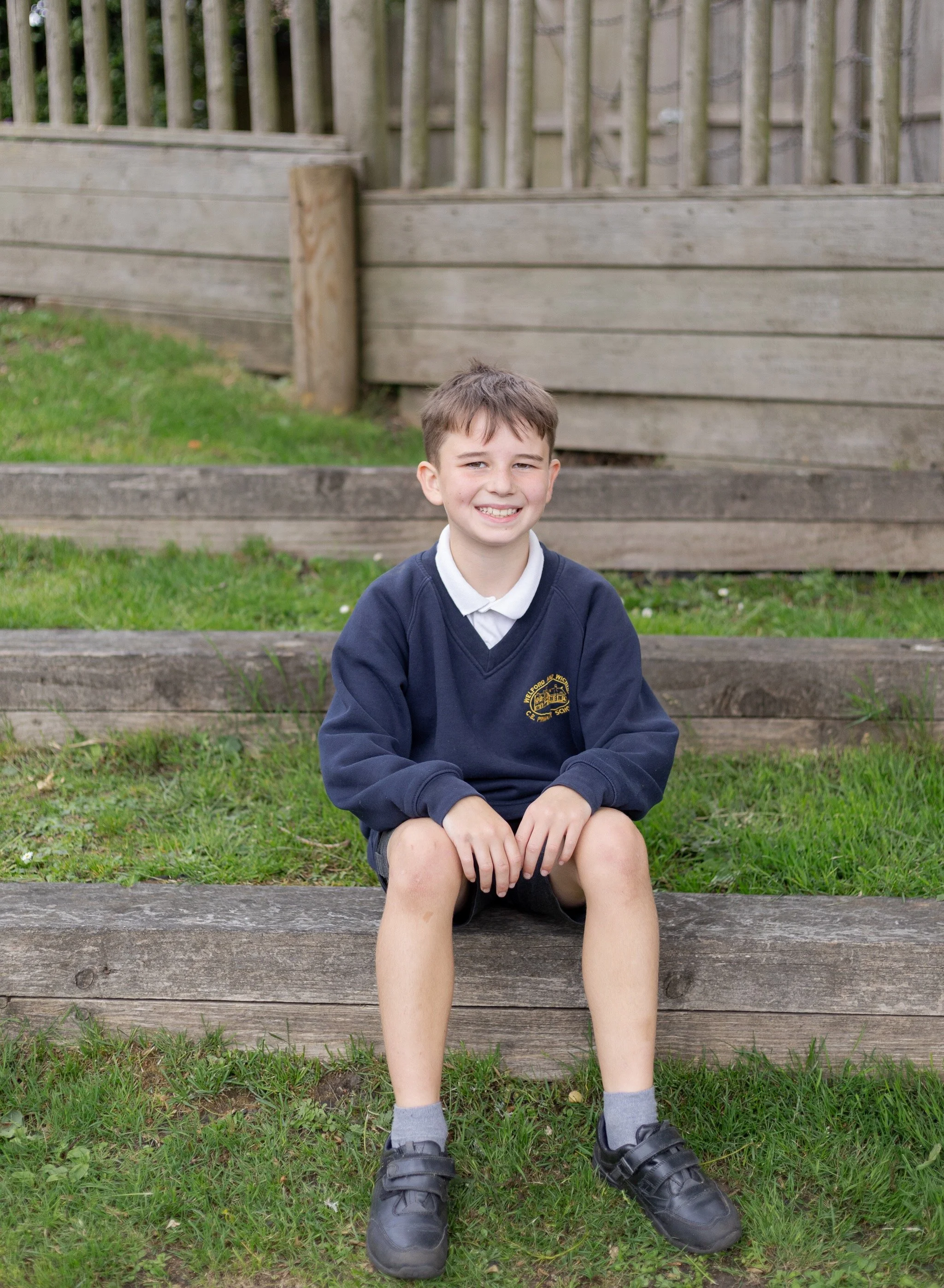 Outdoor school pictures, boy sat outside smiling for school photos. 