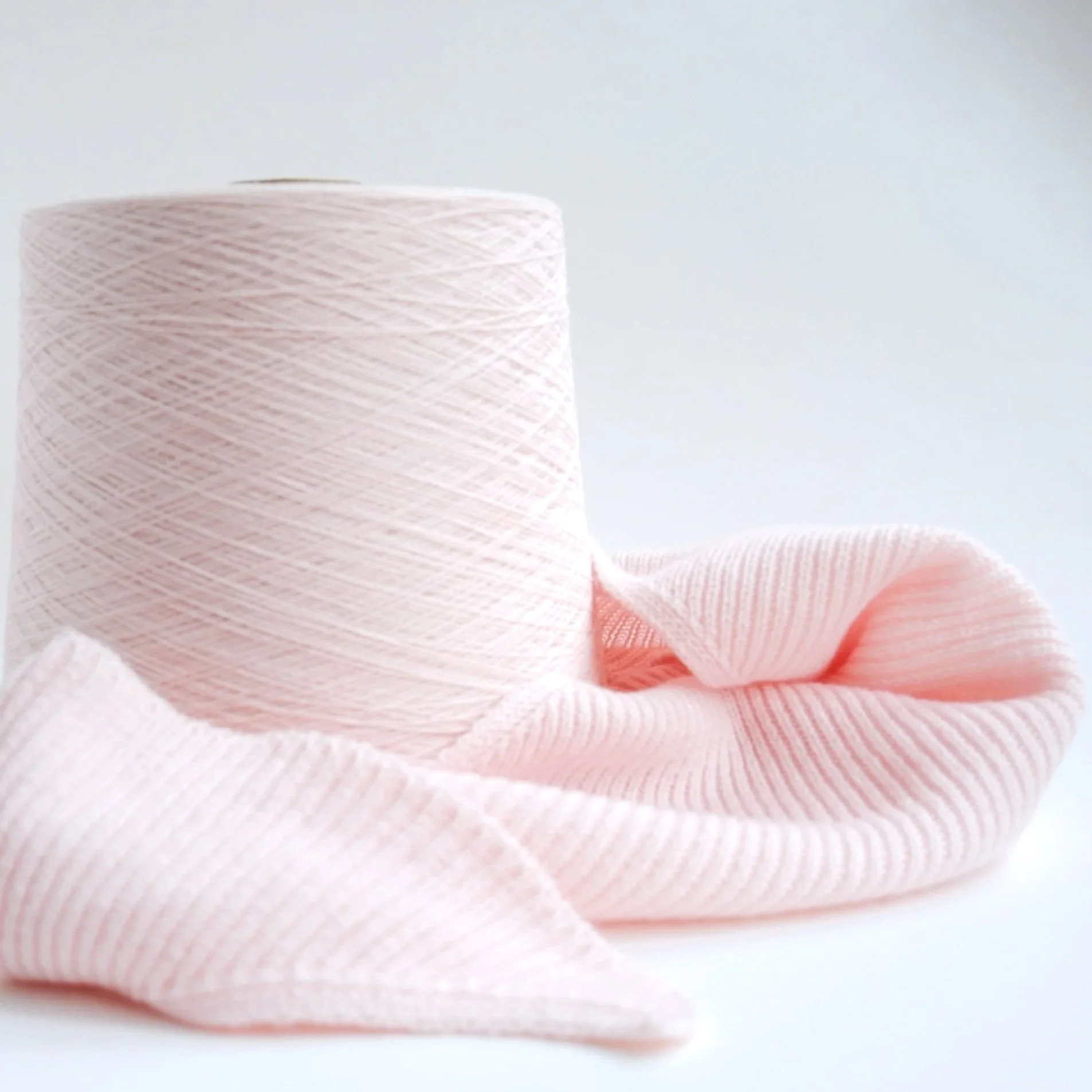 Rouleau de fil de coton rose clair avec une texture en spirale sur un fond blanc.