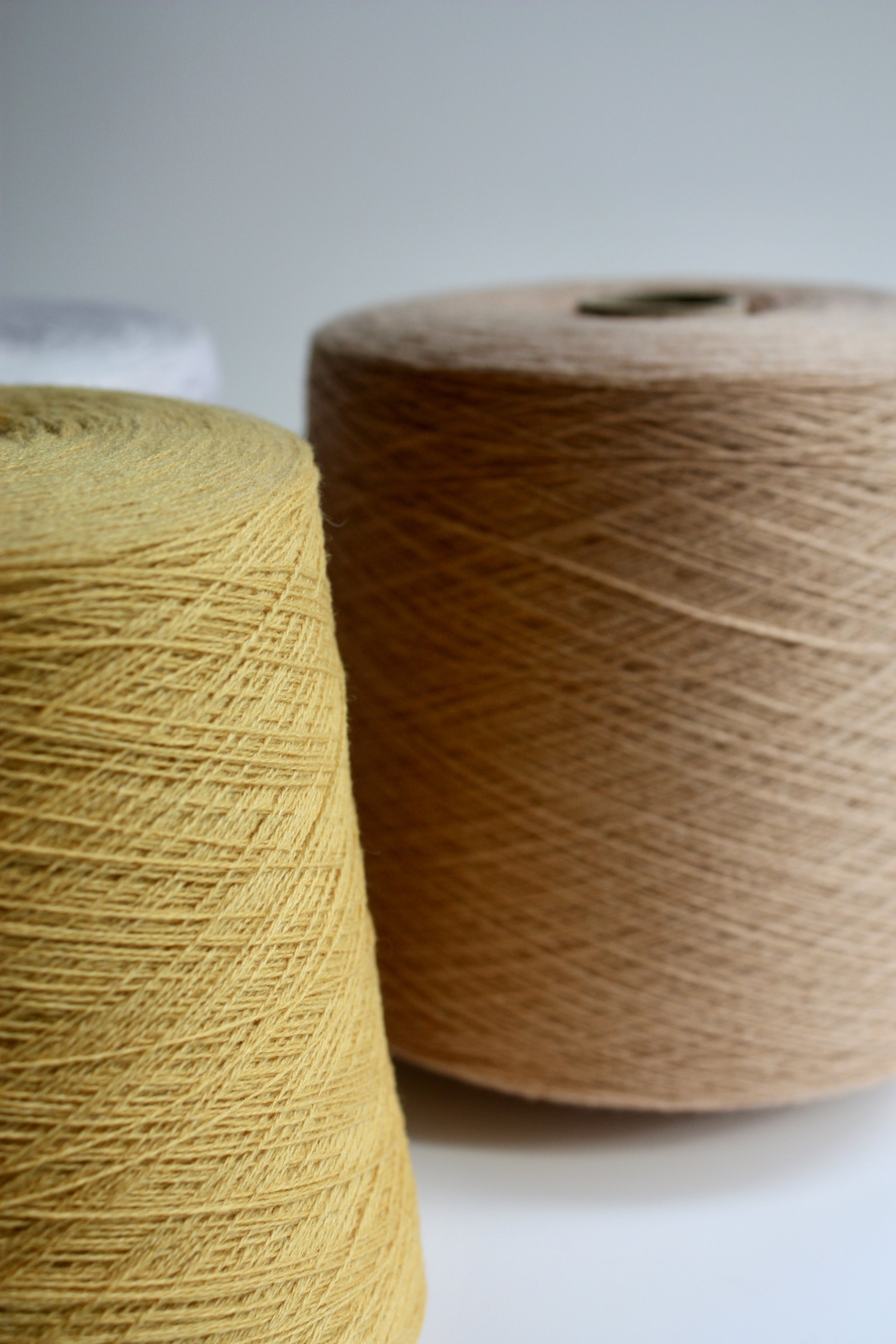 Trois bobines de fil de couleurs différentes, jaune, beige et gris, sur fond blanc.