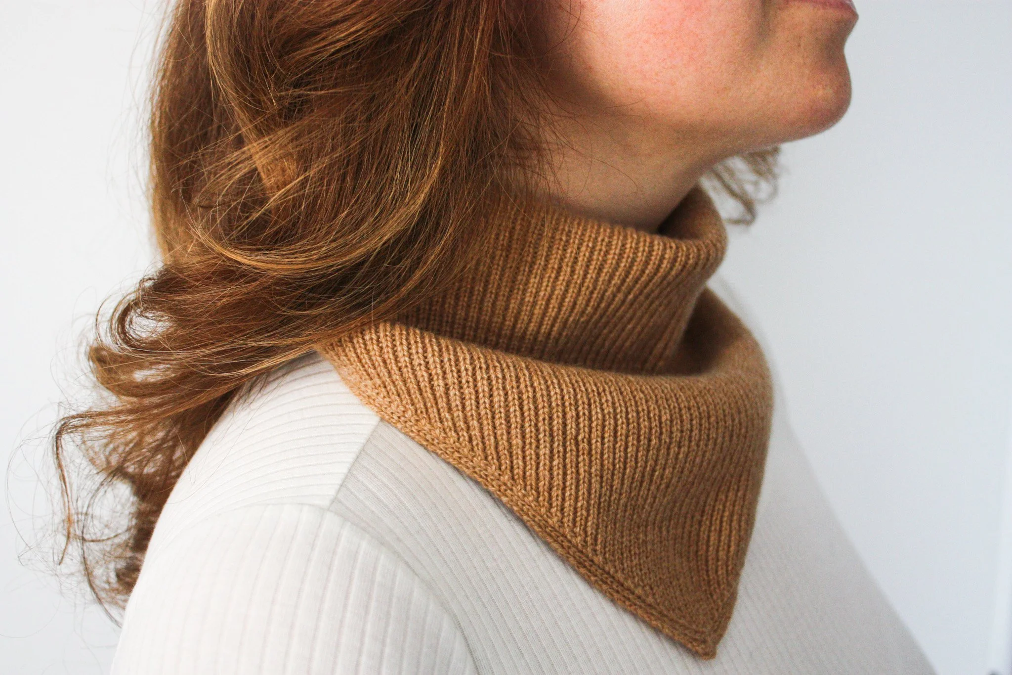 Femme avec des cheveux bouclés roux, portant un foulard beige, en profil côté droit.