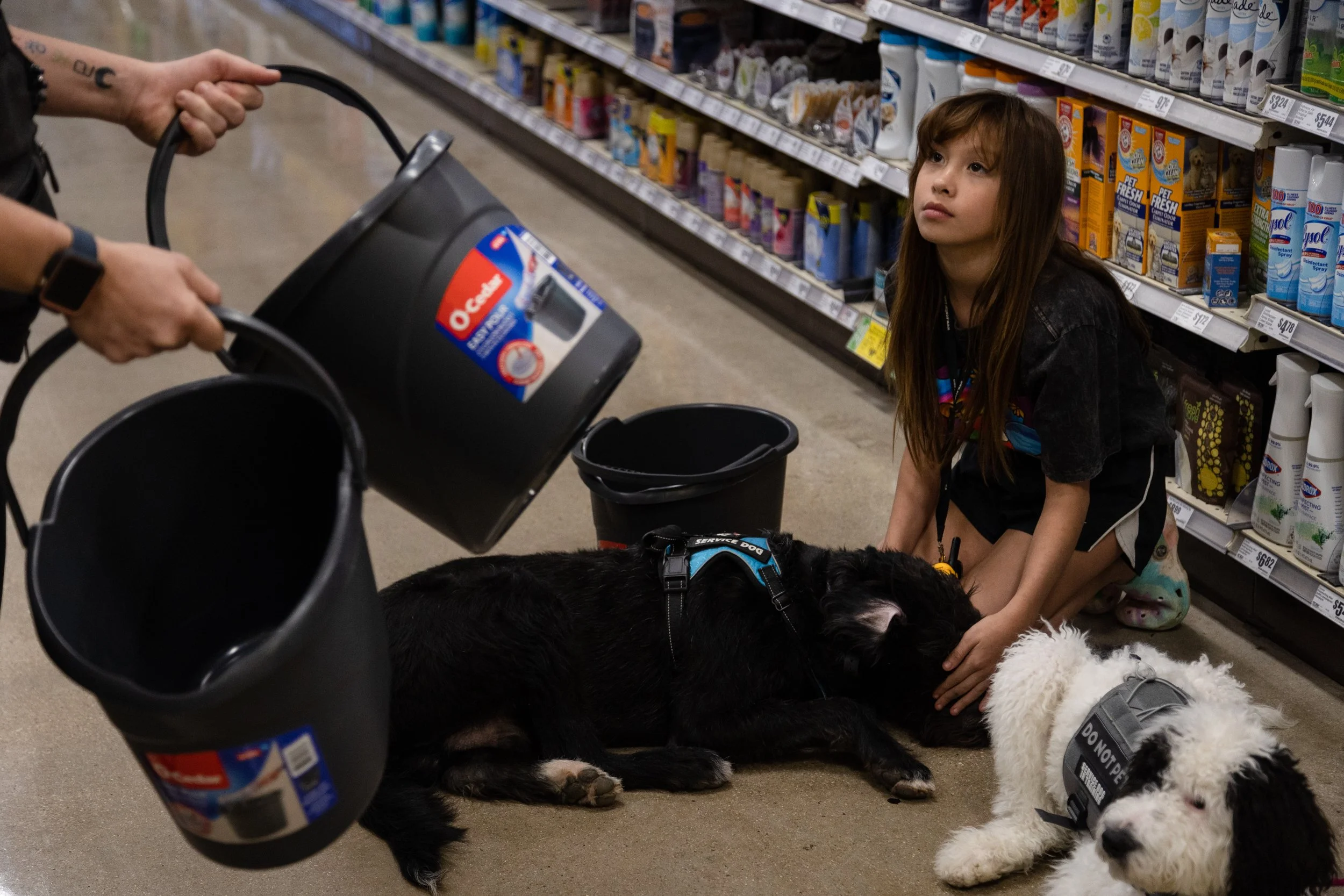  Geneva Story, a trainer with the San Antonio branch of Dog Training Elite, bangs plastic buckets together to make loud noises that might distract Adrianna Medina's therapy dog, Ocean, during training at the local HEB in Uvalde on Nov. 6, 2022. 
