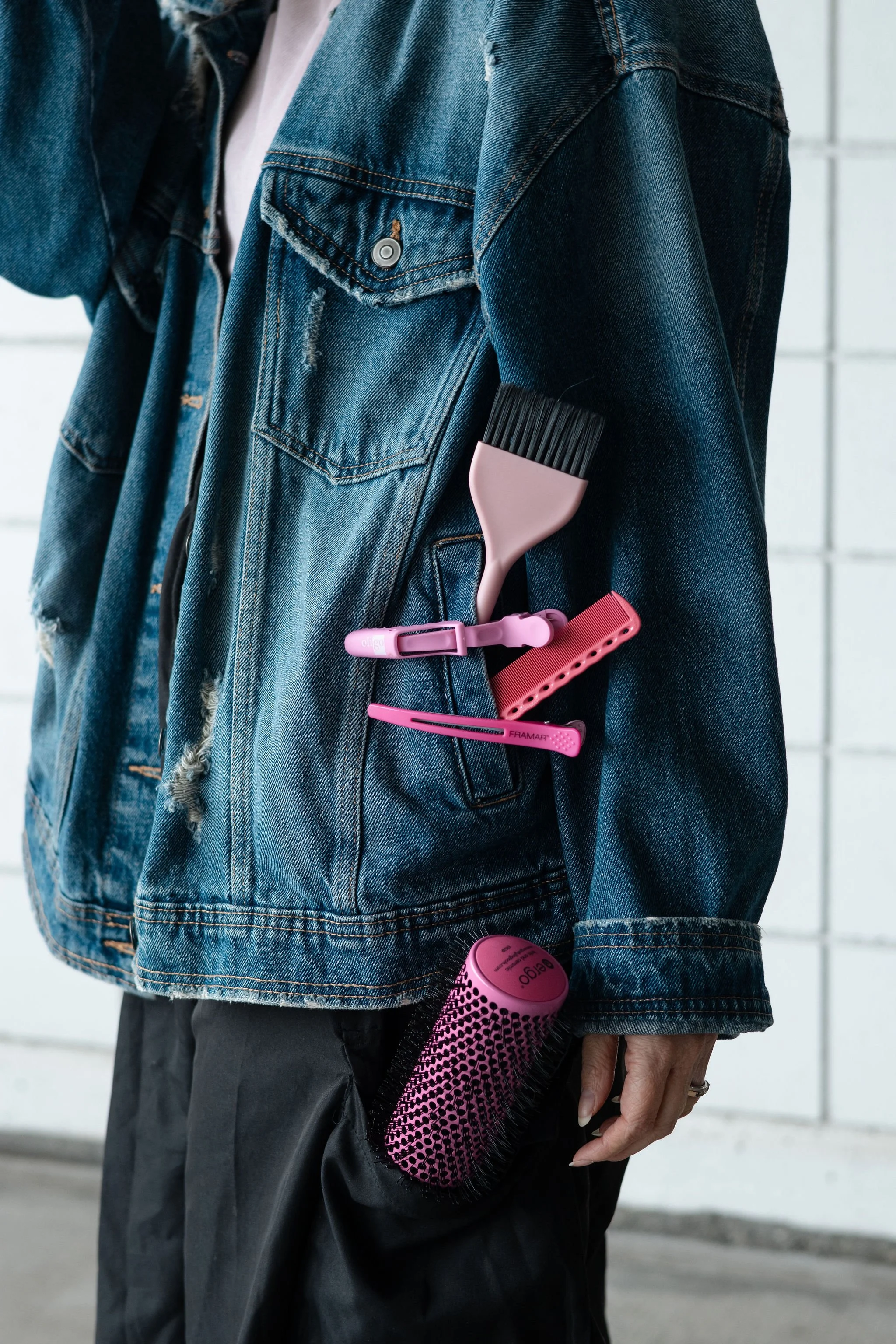 Person wearing a blue denim jacket with pink and black personal care accessories attached to the pocket..The salon offers a range of services including haircuts, coloring, styling.