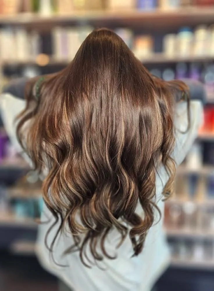 Back of a person with long, wavy, brown hair blended hair extensions.