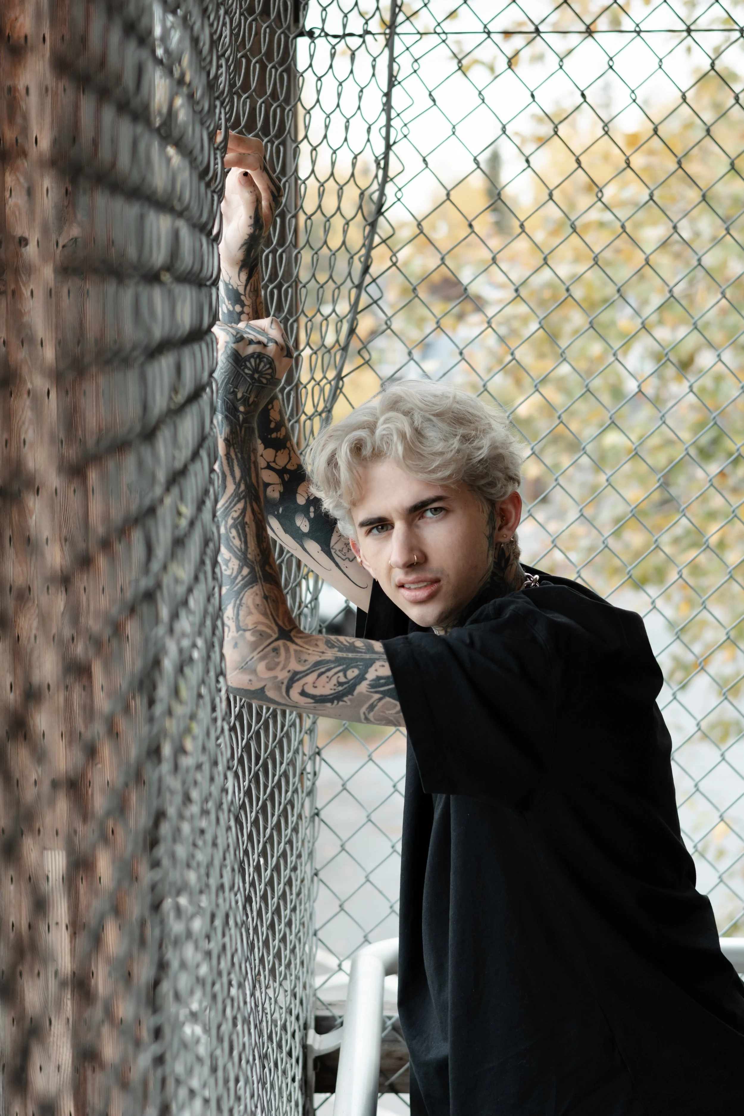 Portrait of a young person with blond hair & tattoos on their arms. .Professional blonde hair color services at Misfits Salon in Anchorage, Alaska, specializing in platinum blondes, dimensional highlights, lived in blonding, balayage, & custom Blonde