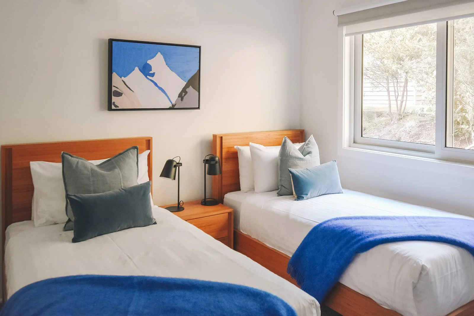 Twin guest bedroom featuring timber bed frames, blue bedding accents and Australian landscape inspired artwork.