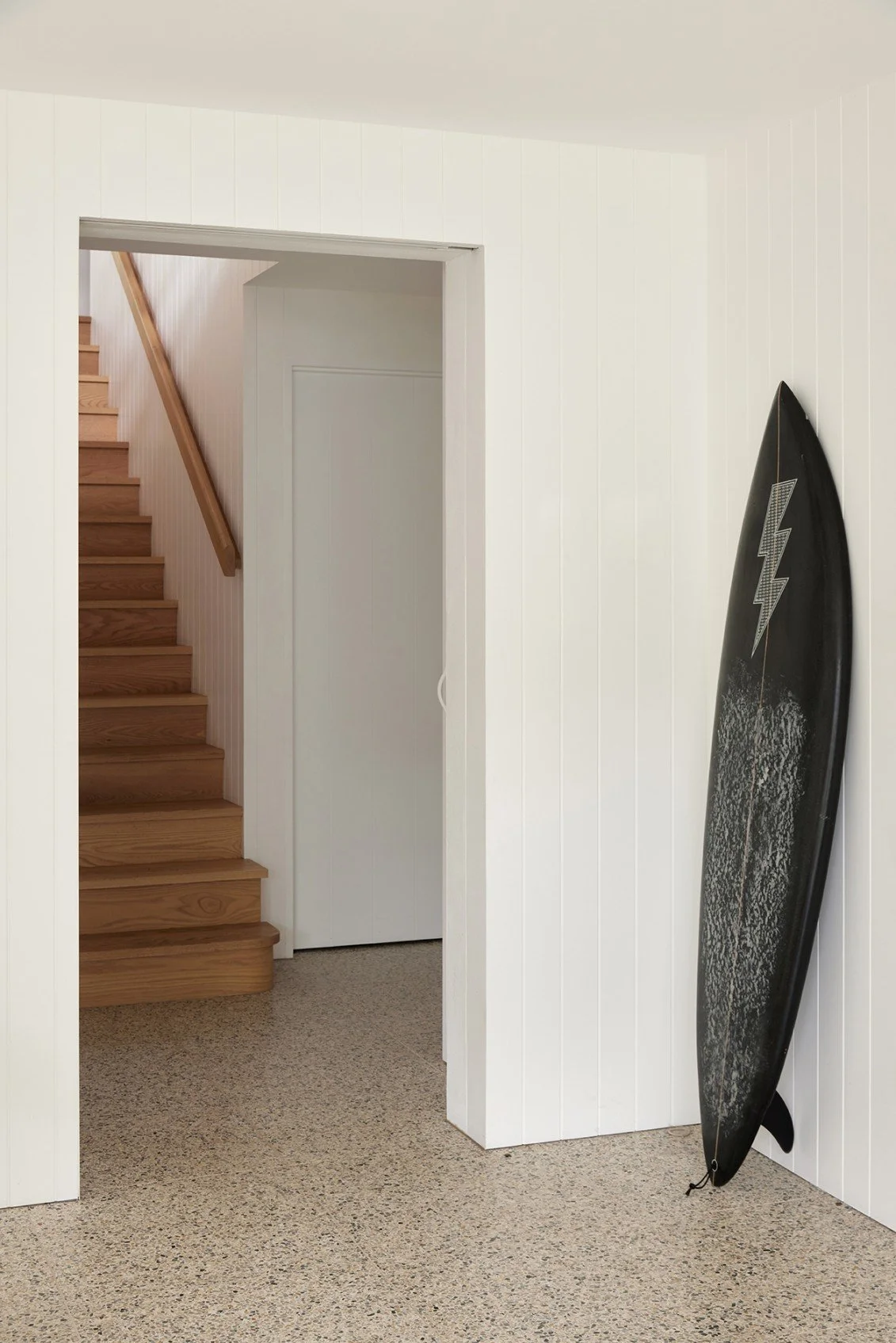 Stairs to the basement level, featuring surfboard storage