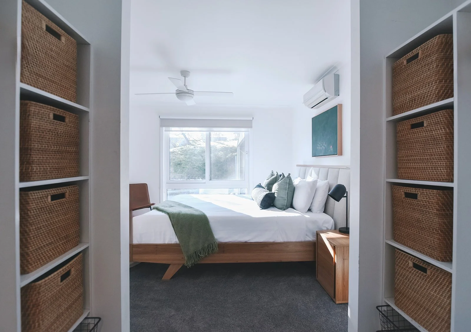 Main bedroom framed by practical open storage, featuring natural timber furniture, soft green furnishings and a calm neutral palette.