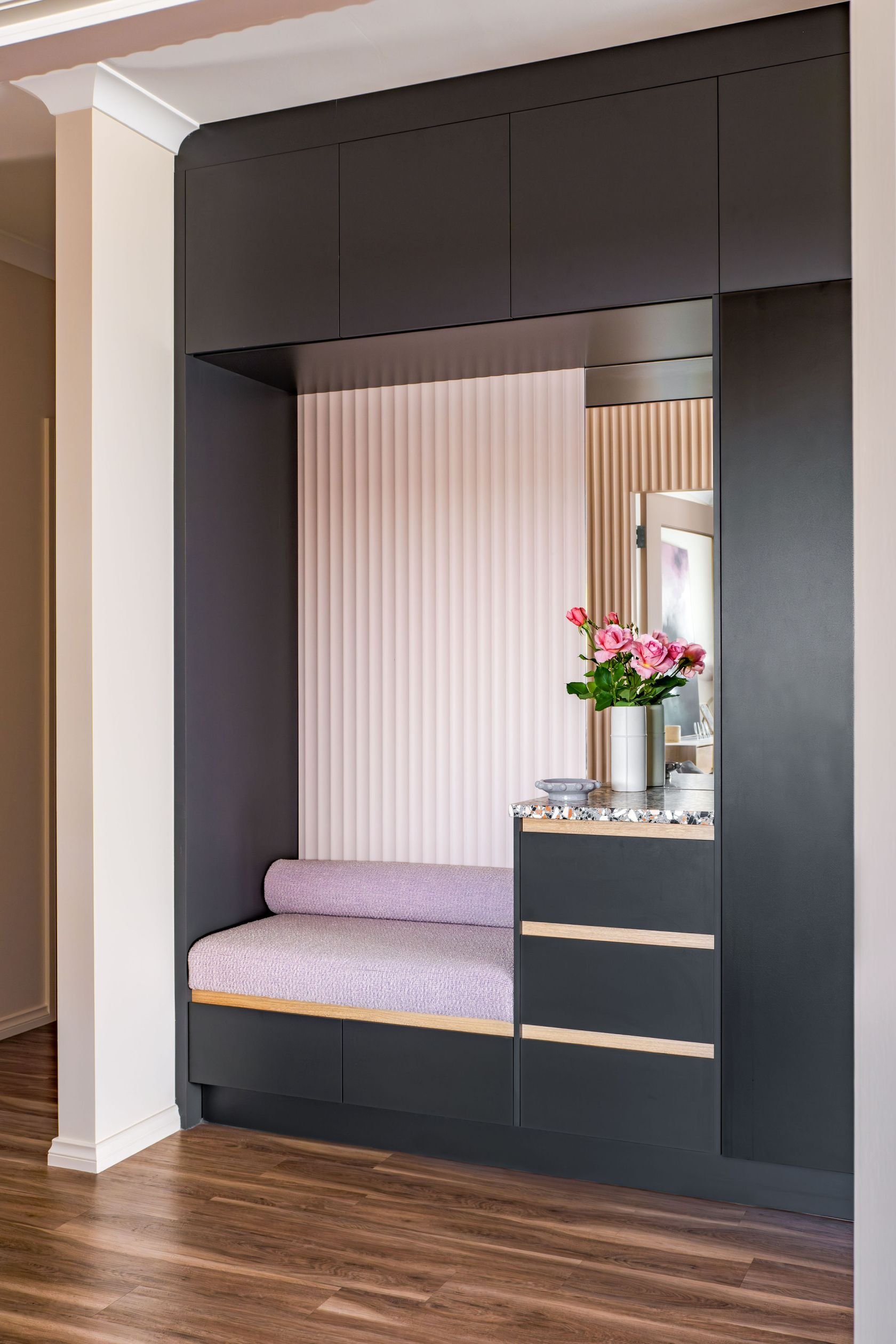 Custom joinery with integrated storage and seating, repurposes a disused niche upon entry, at the start of the pink ribbon that runs through the house.