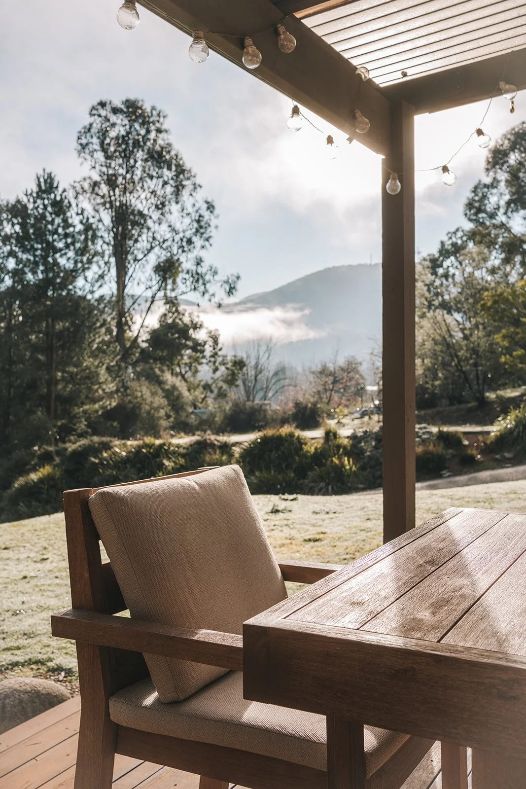 Covered outdoor entertaining area at Alpine Gum featuring generous timber framed lounge seating, neutral cushions and views of the surrounding bushland.