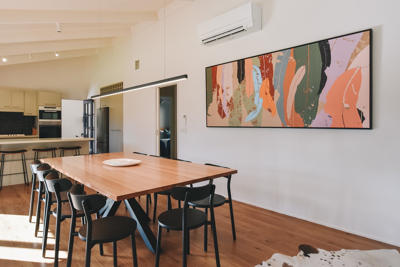 Alpine Gum dining room with a repurposed timber tabletop, sculptural black metal base, Design By Them dining chairs and vibrant Australian artwork.