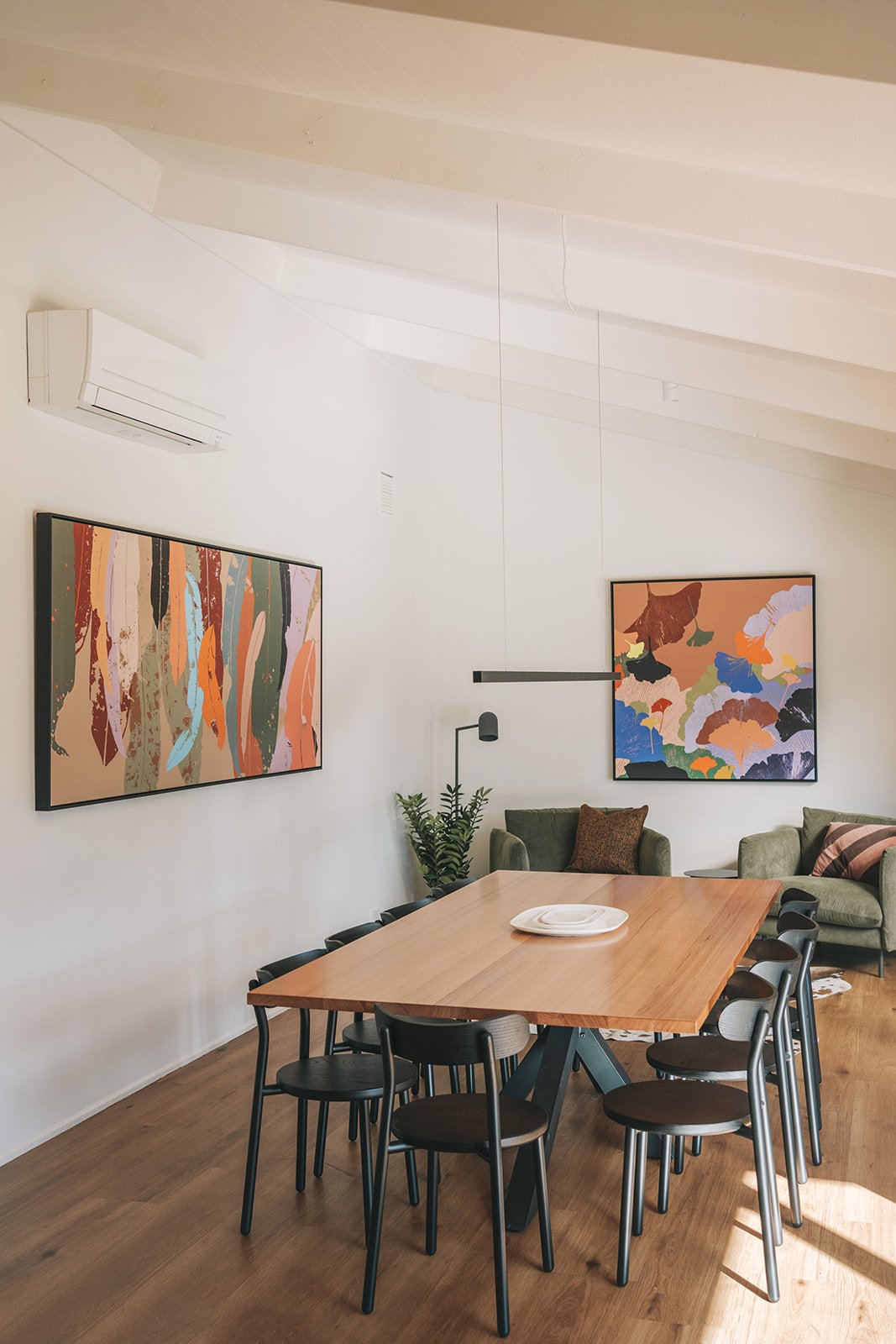 Light filled dining room with colourful abstract artwork, a contemporary linear pendant light and timber dining table.