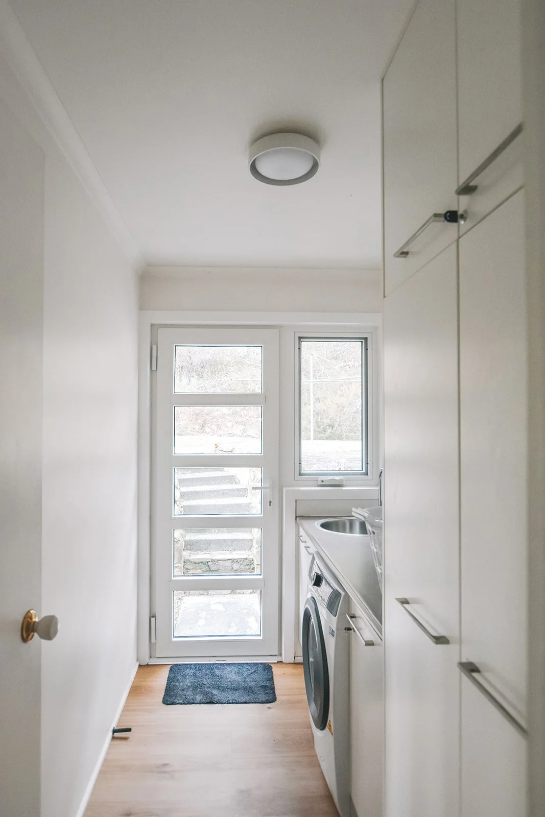 Functional holiday home laundry with integrated cabinetry, washing machine, storage, new light fixture and natural light.