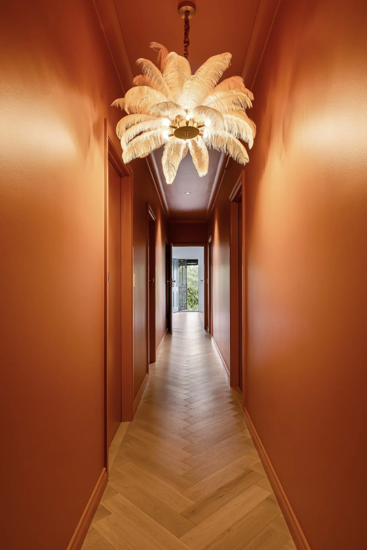 A chevron floor, feather pendant and the rust colour drenched hallway draw the eye towards the bedrooms, main bathroom and the more expressive rooms beyond.