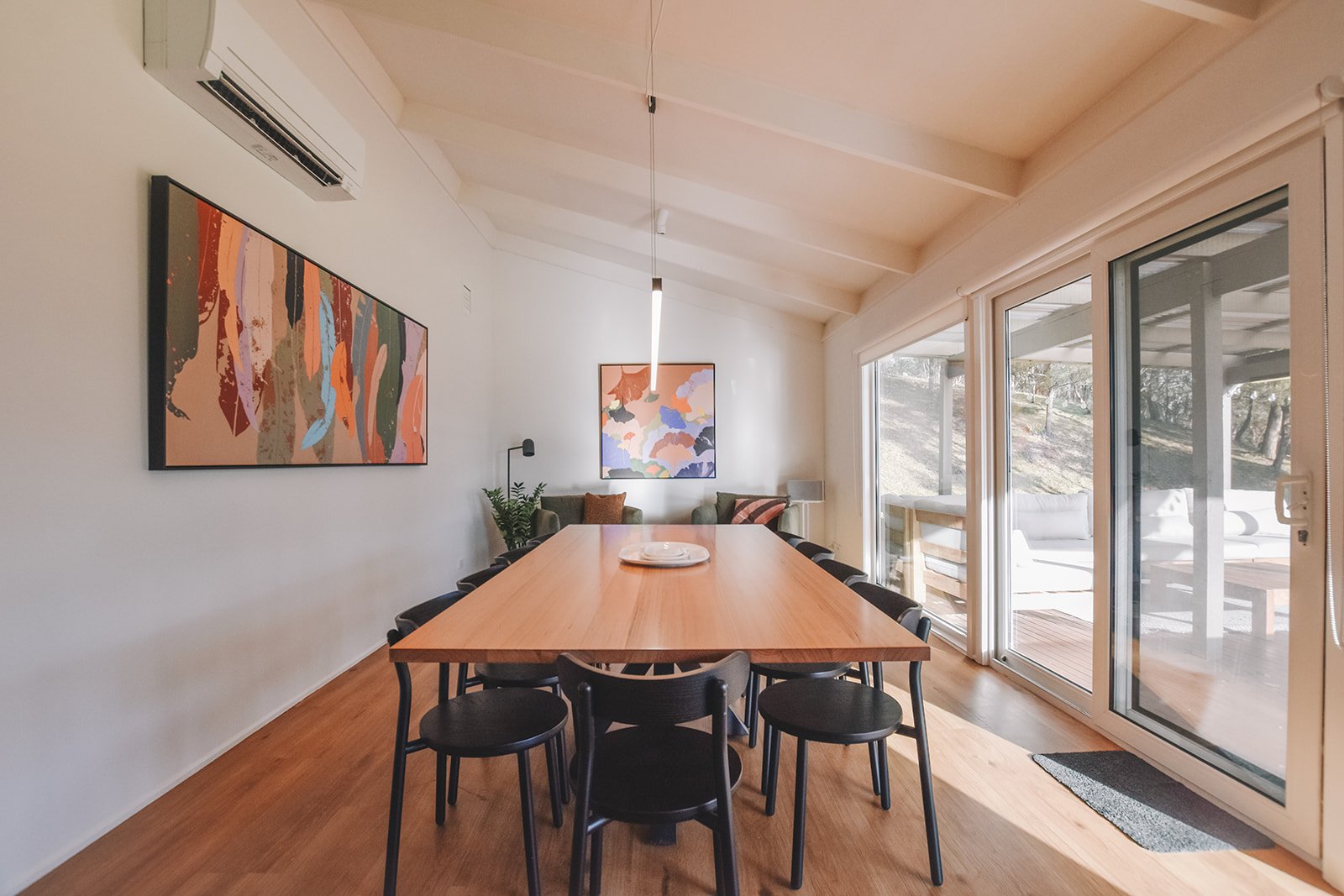 Light filled dining room at Alpine Gum featuring a timber dining table, contemporary black chairs, colourful Australian artwork and views to the outdoor entertaining area.