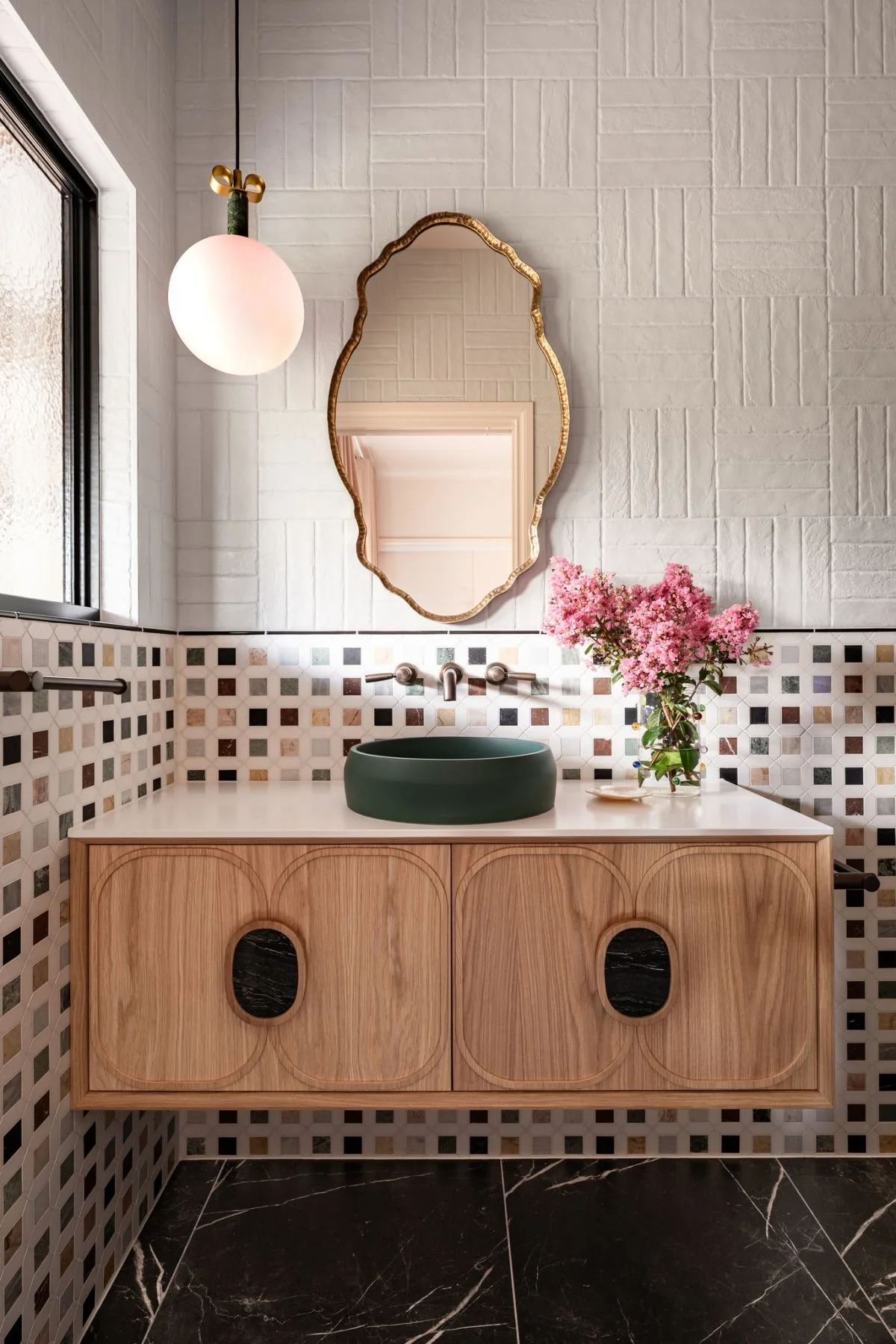 The ensuite features the same mosaic wall tiles from the kitchen, sculptural gold mirrors and a black concrete basin atop an American oak Zuster vanity that brings warmth and craft. 

