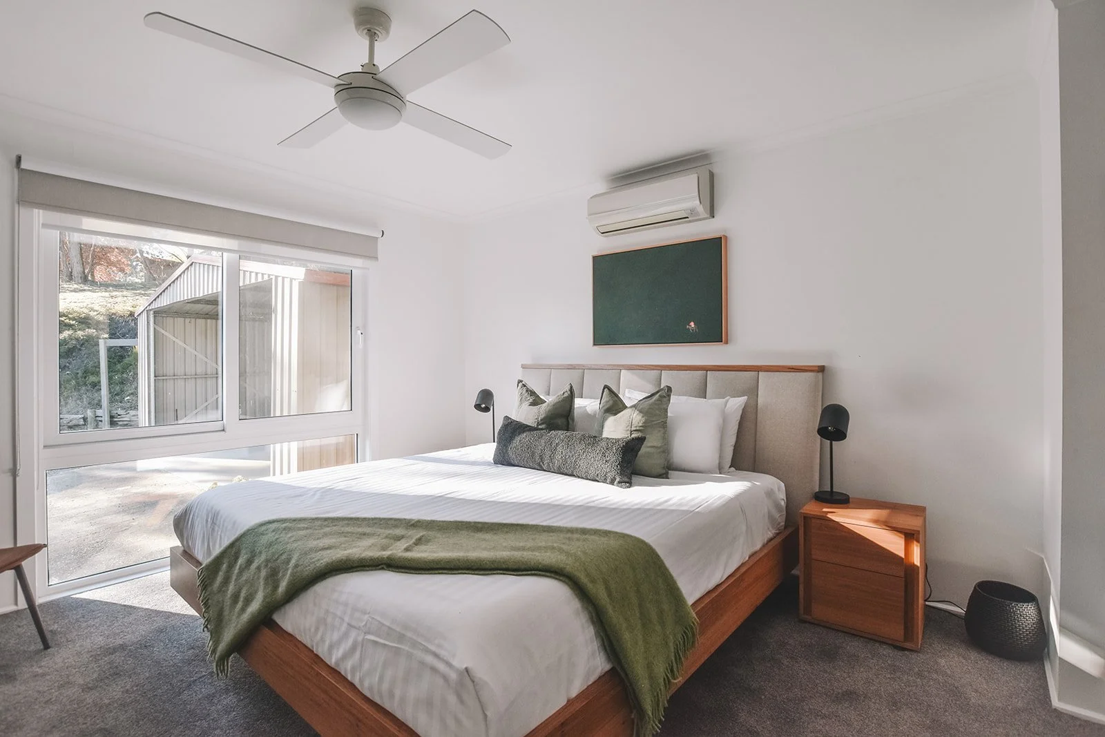 Contemporary guest main bedroom featuring a timber bed frame, upholstered headboard, soft green textiles and carefully curated artwork.