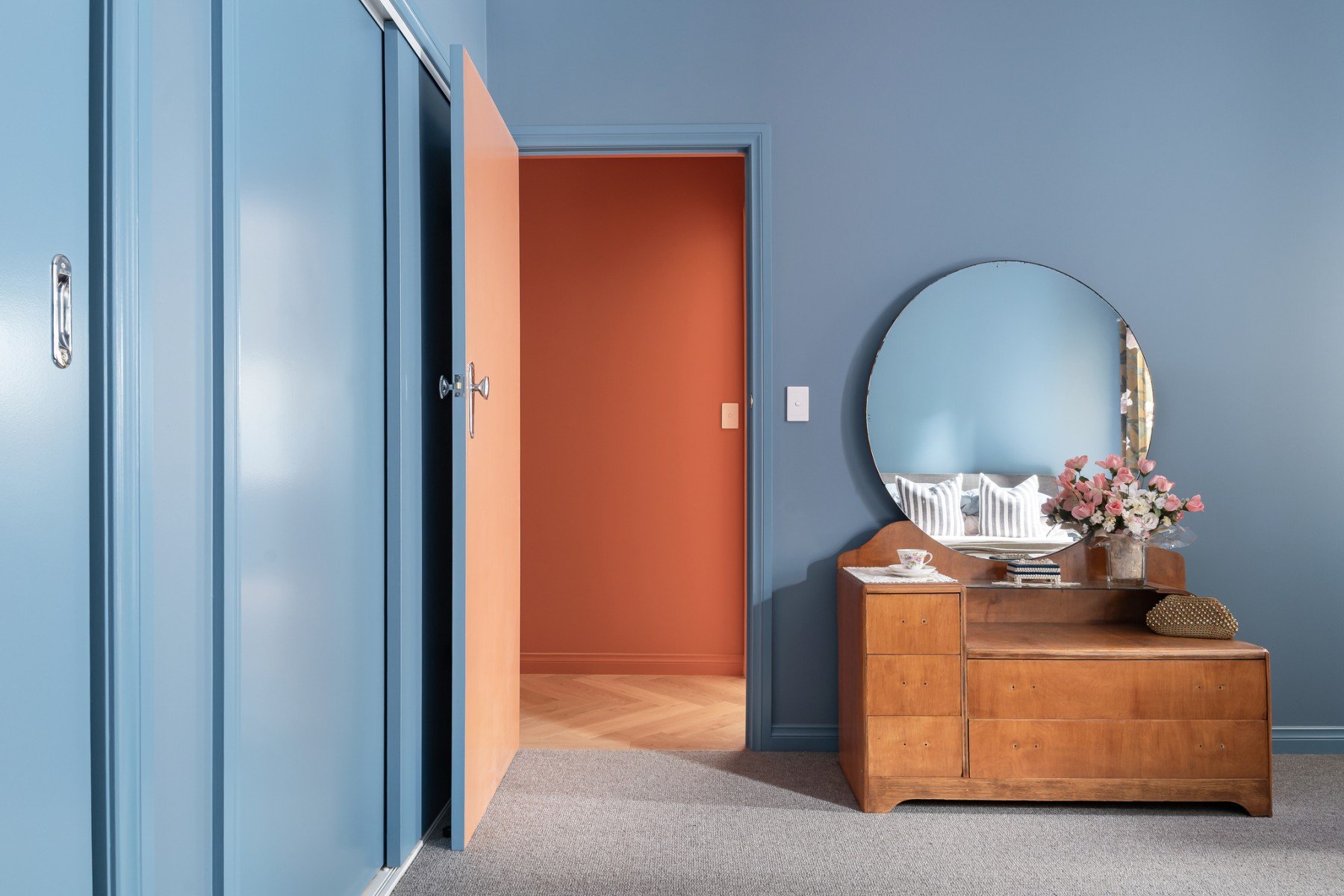 In the bedrooms, the palette softens with sky blue walls, botanical wallpaper, dusky pinks and rust accents, vintage furniture and layered textiles.