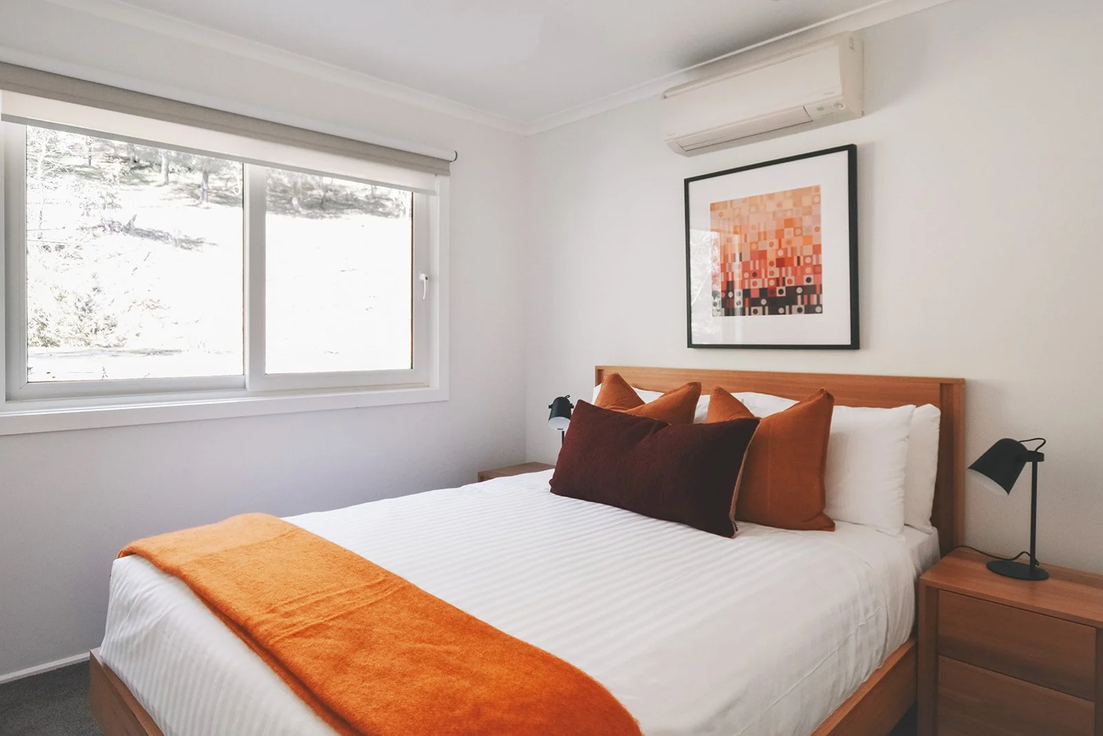 Guest bedroom with warm orange and rust coloured textiles, natural timber furniture and geometric artwork.