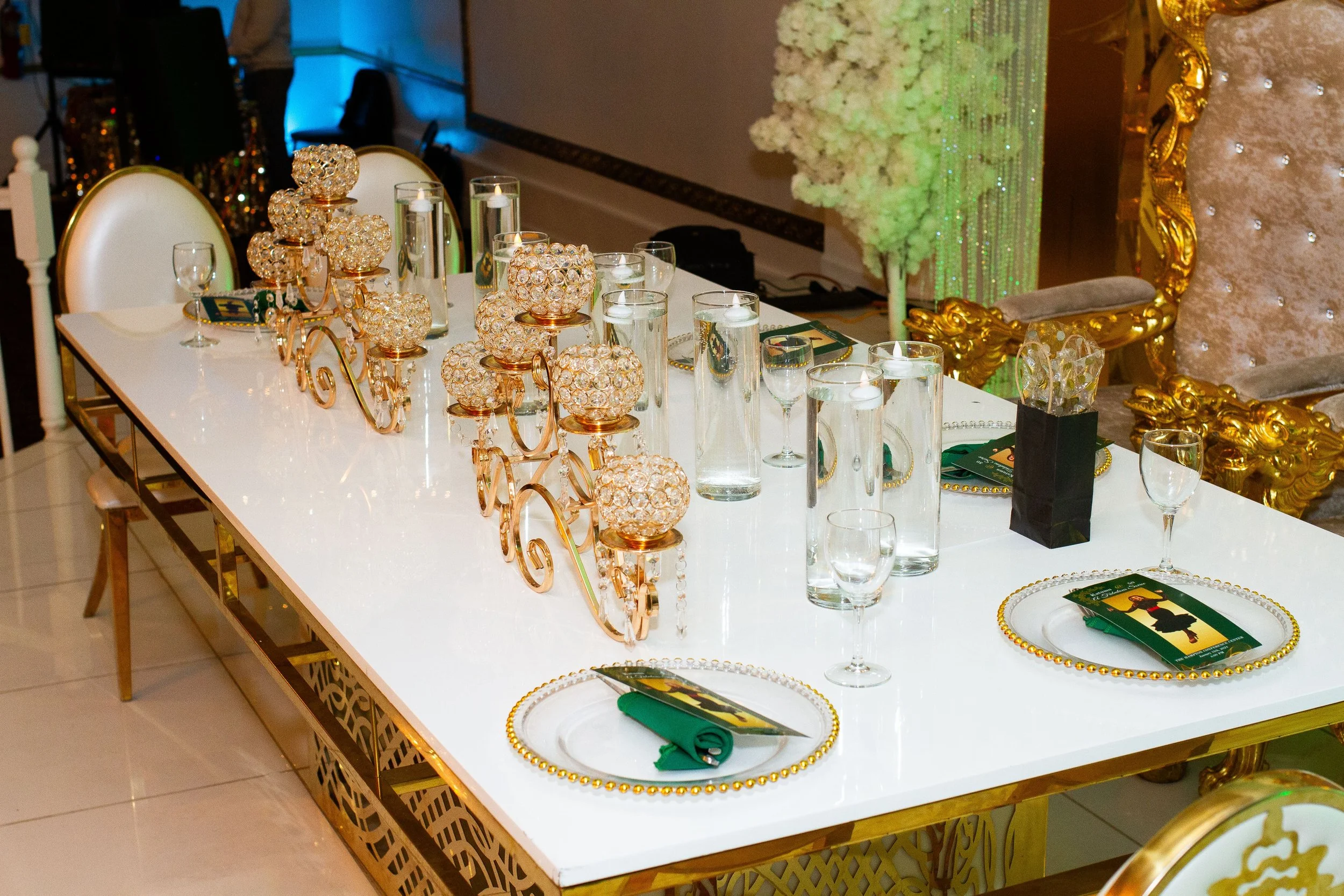 Decorated banquet table with gold accents, candles, water glasses, and elegant place settings for a celebration or event.