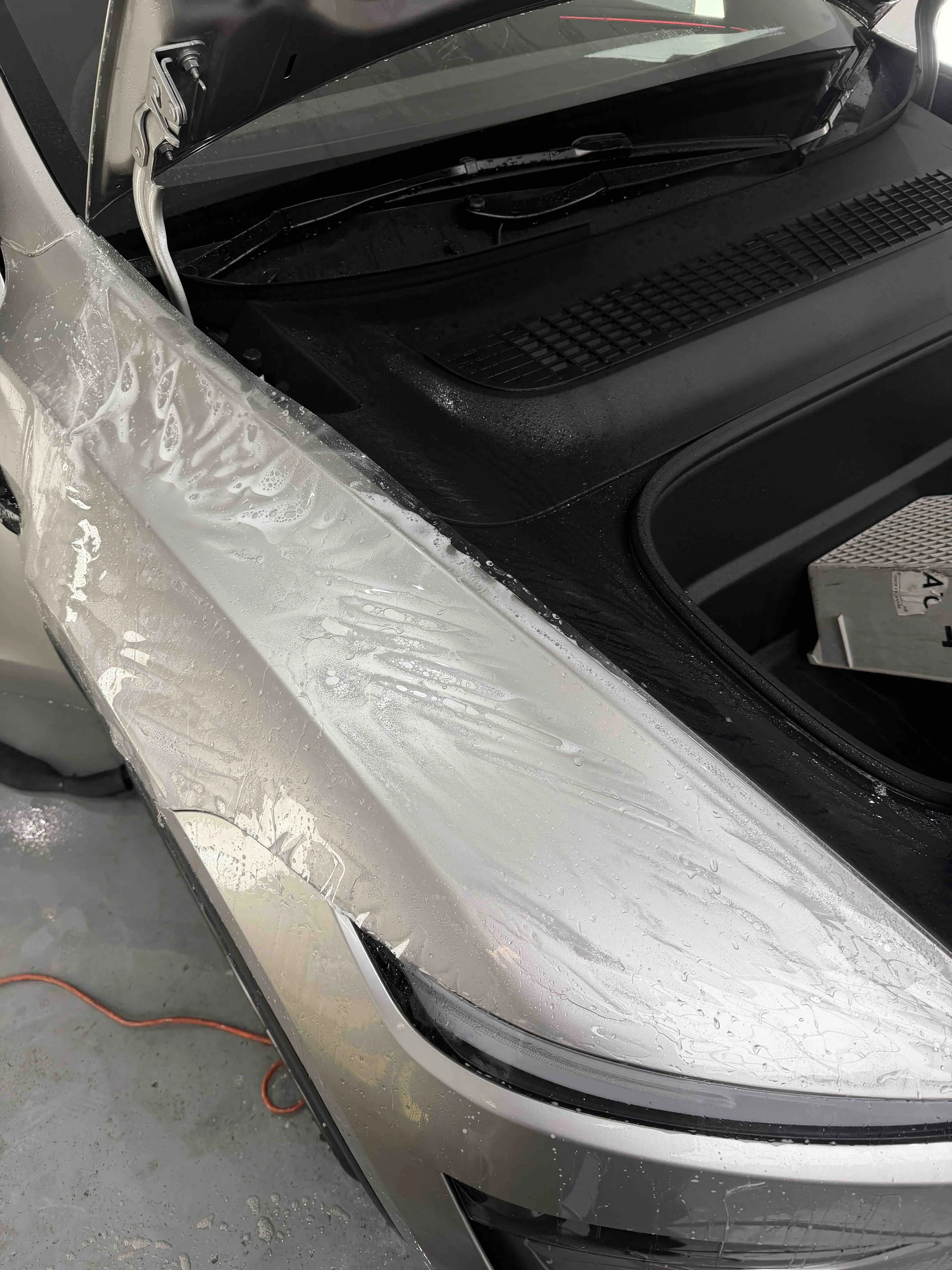Close-up of a wet silver car hood, windshield wipers, and windshield cowl during detailing.