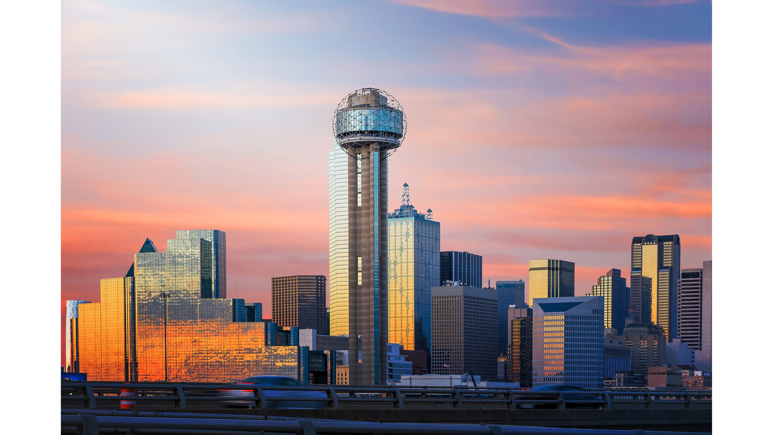 City skyline at sunset featuring a tall tower with a spherical top and surrounding modern glass buildings.
