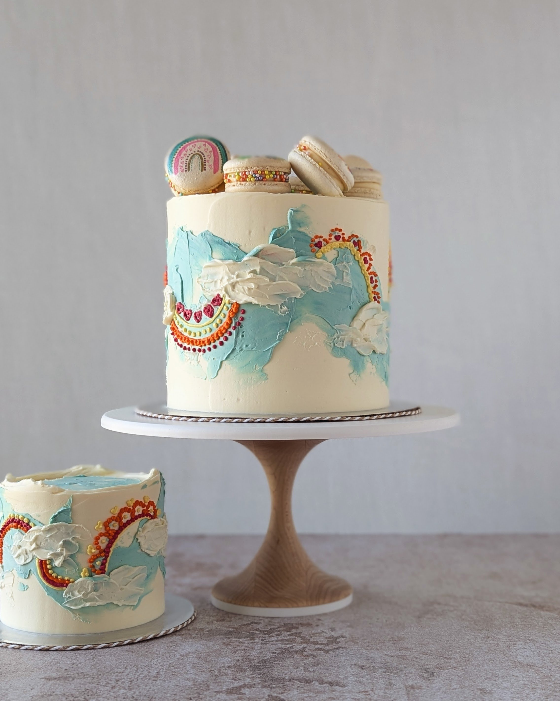 A 6 inch rainbow themed cake with hand painted macarons and a matching 4 inch cake.