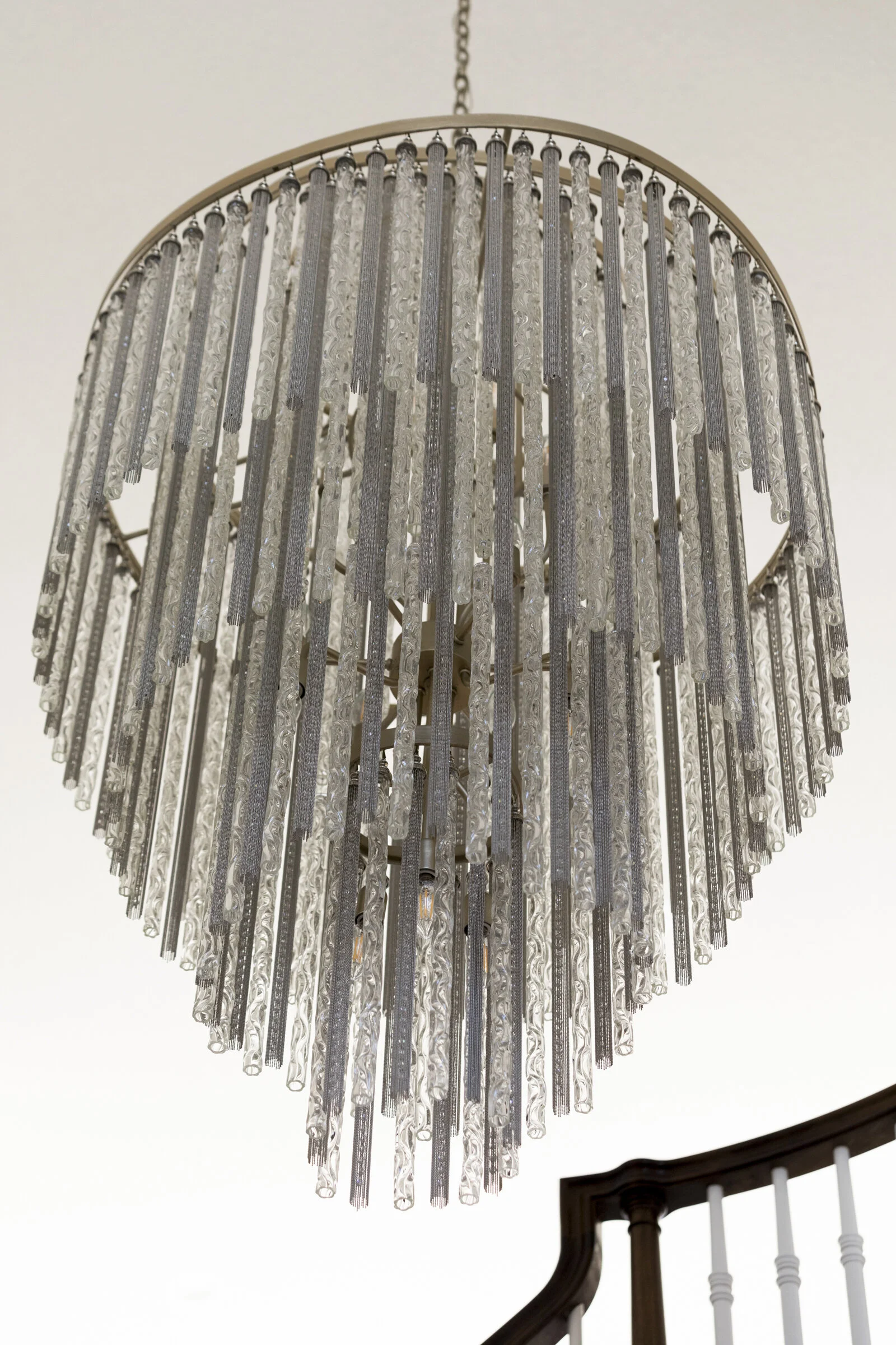 Elegant chandelier with hanging crystals, mounted on ceiling above staircase.