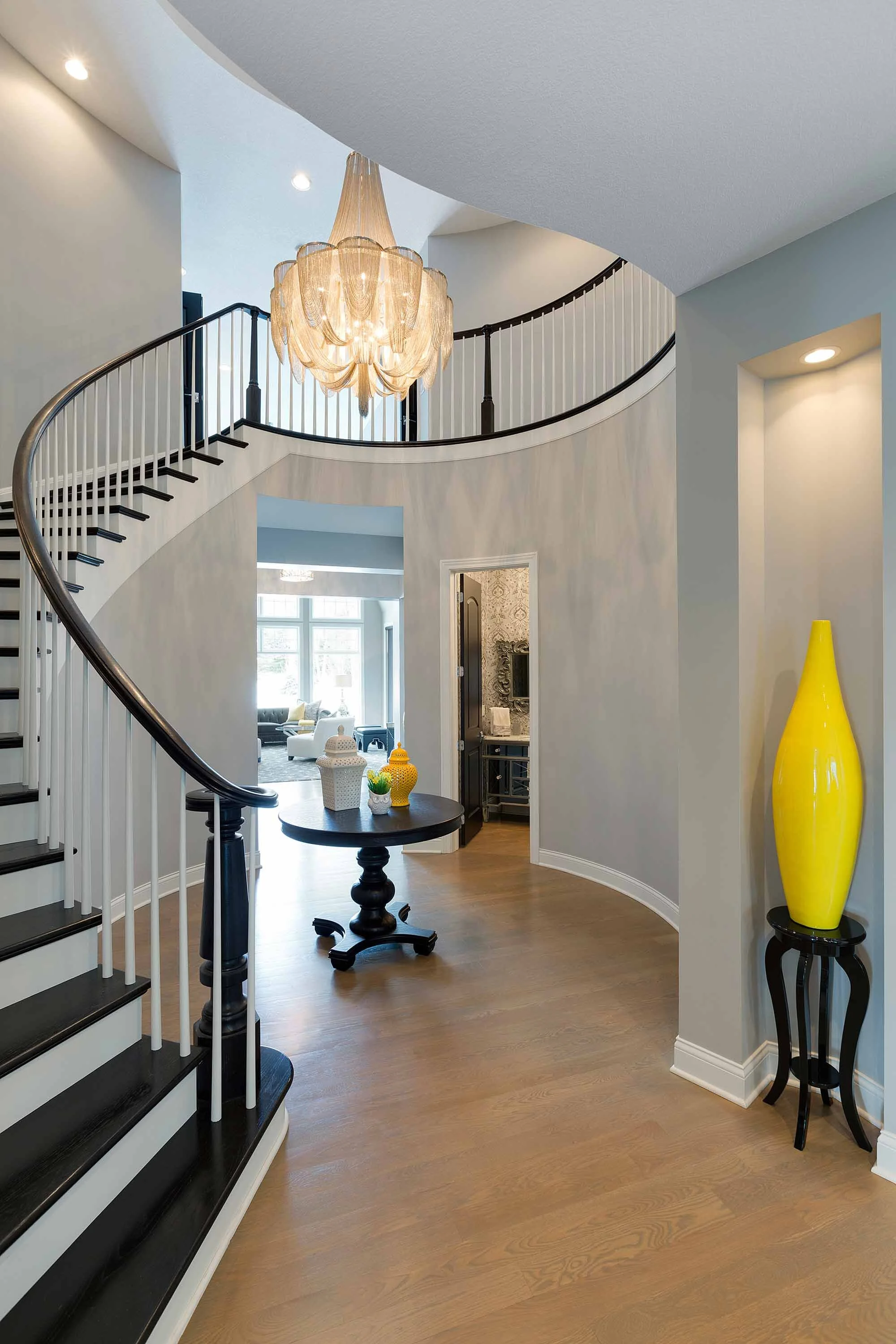 Elegant foyer with spiral staircase, chandelier, and yellow vase decor.
