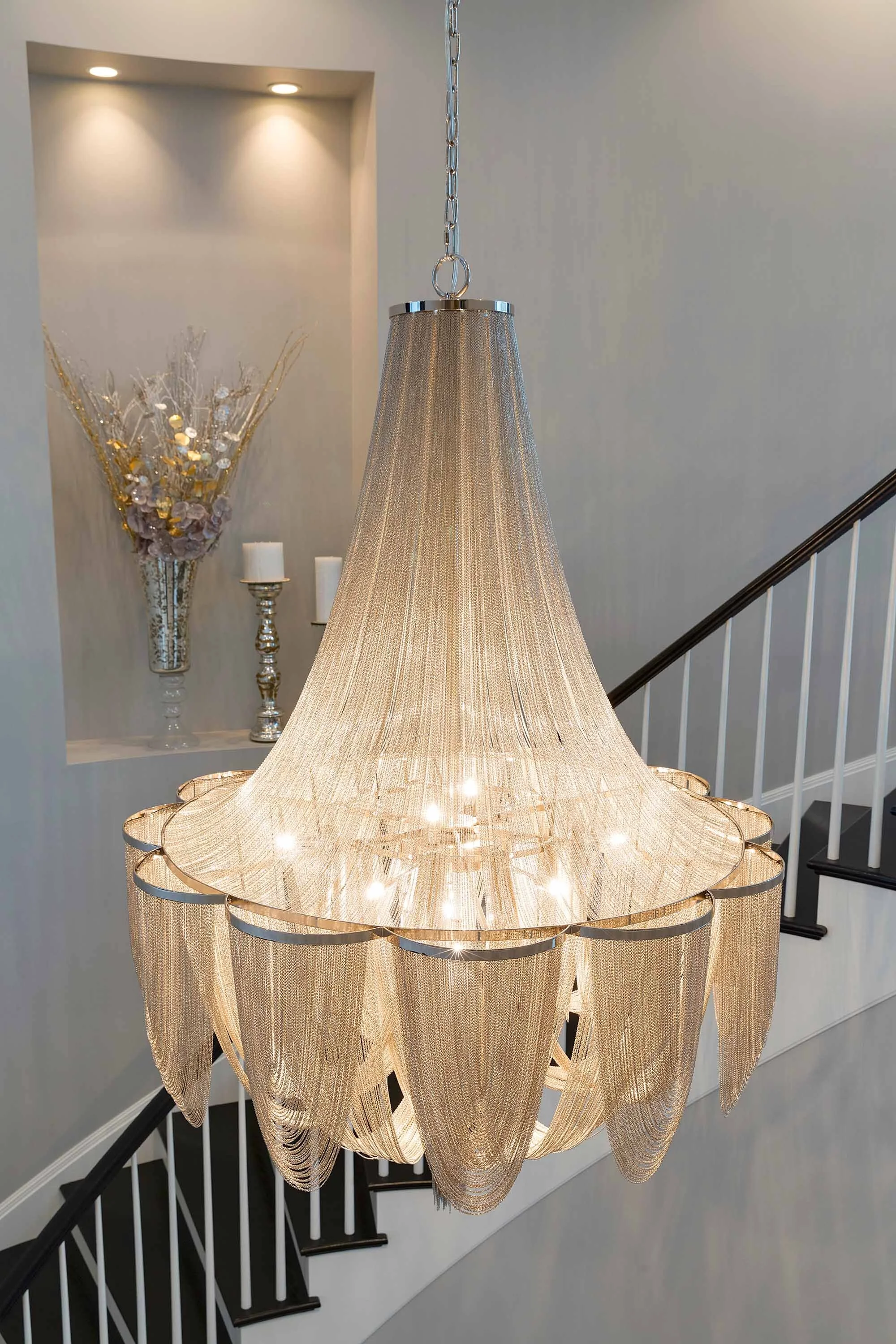 Elegant chandelier with a gold and crystal design hanging in a modern foyer with stairs and decorative wall art.