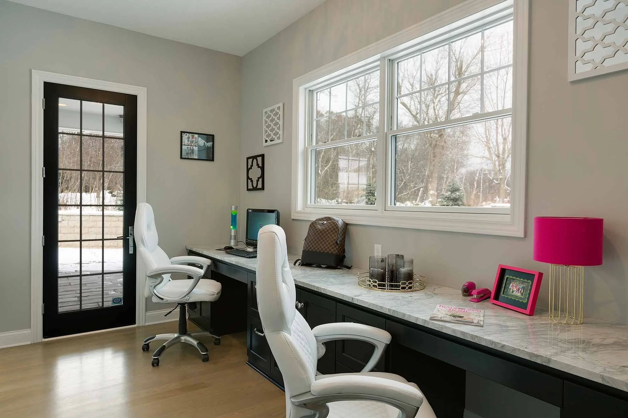 Home office with a marble desk, white chairs, window view of snow outside, and decorative items like a pink lamp and picture frame.