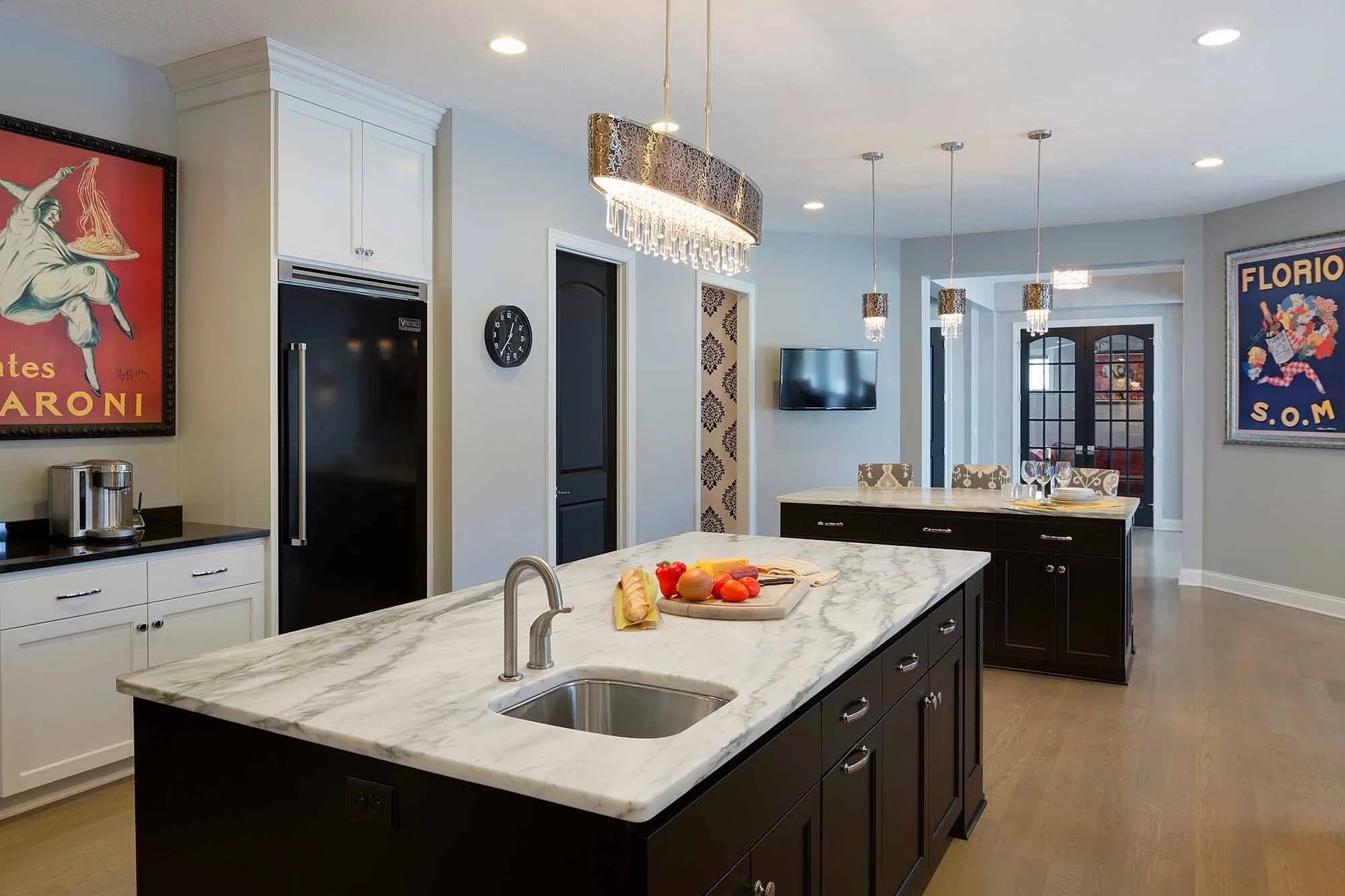 Modern kitchen with black and white cabinetry, marble island with a sink, pendant lights, wall art, and a refrigerator.