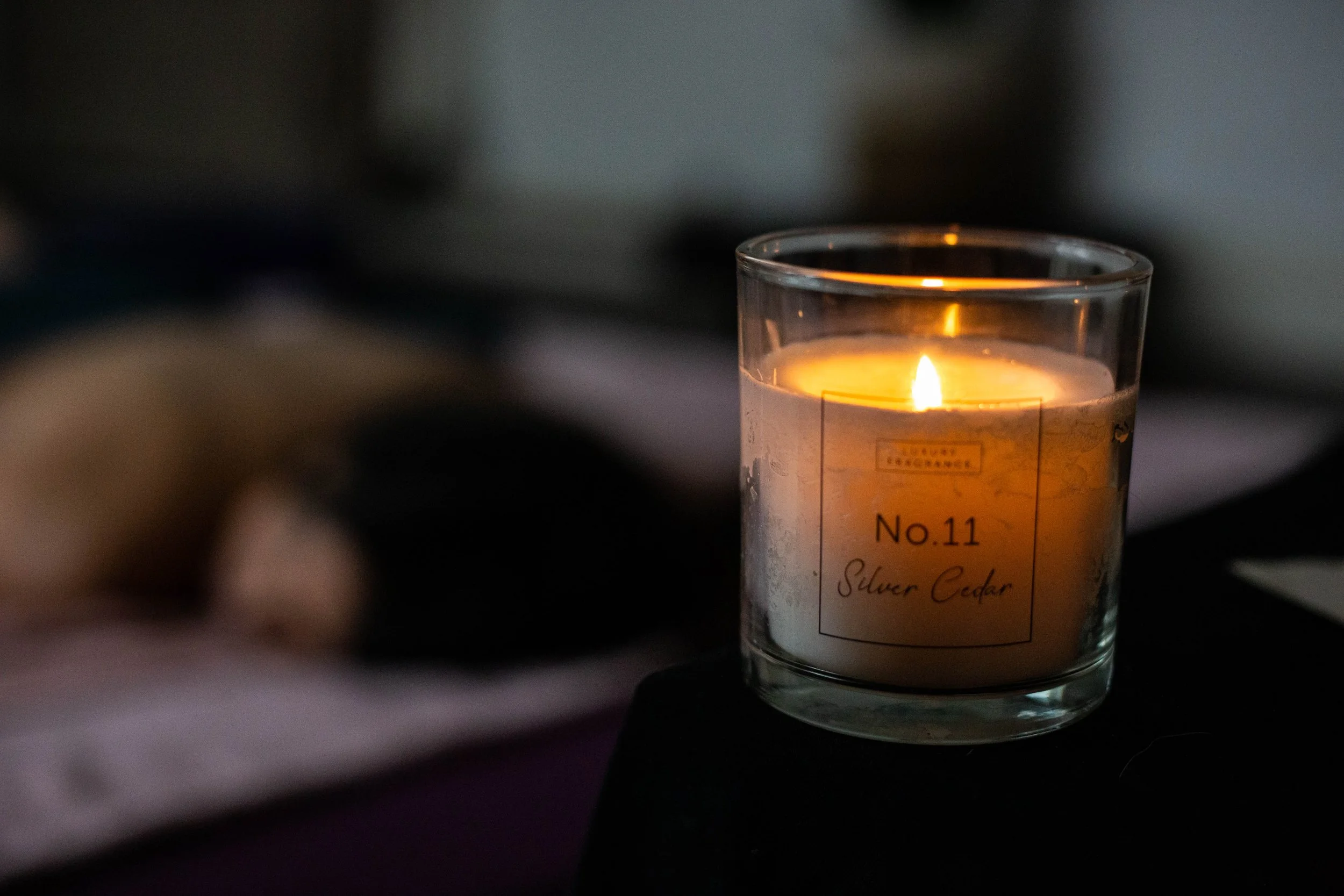 A lit candle in a glass container labeled 'No.11 Silver Cedar' on a dark background.