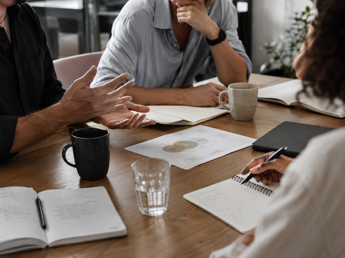 Team members in discussion around a table with notebooks and documents during a collaborative conversation.
