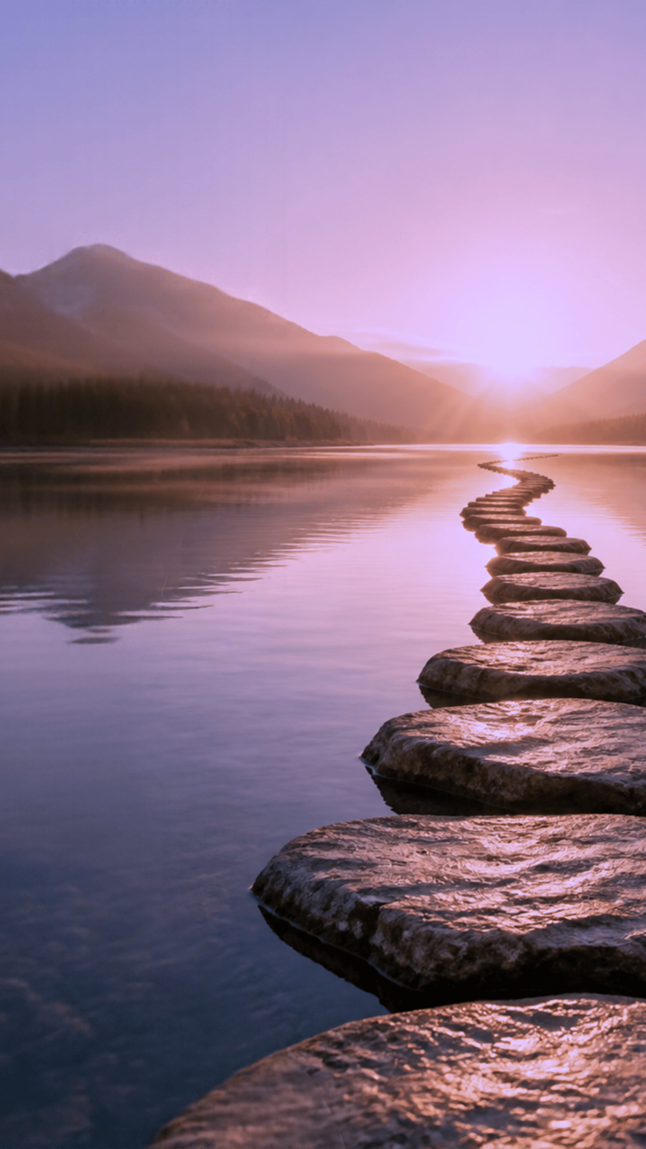 Stepping stones crossing a calm lake toward misty mountains at sunset